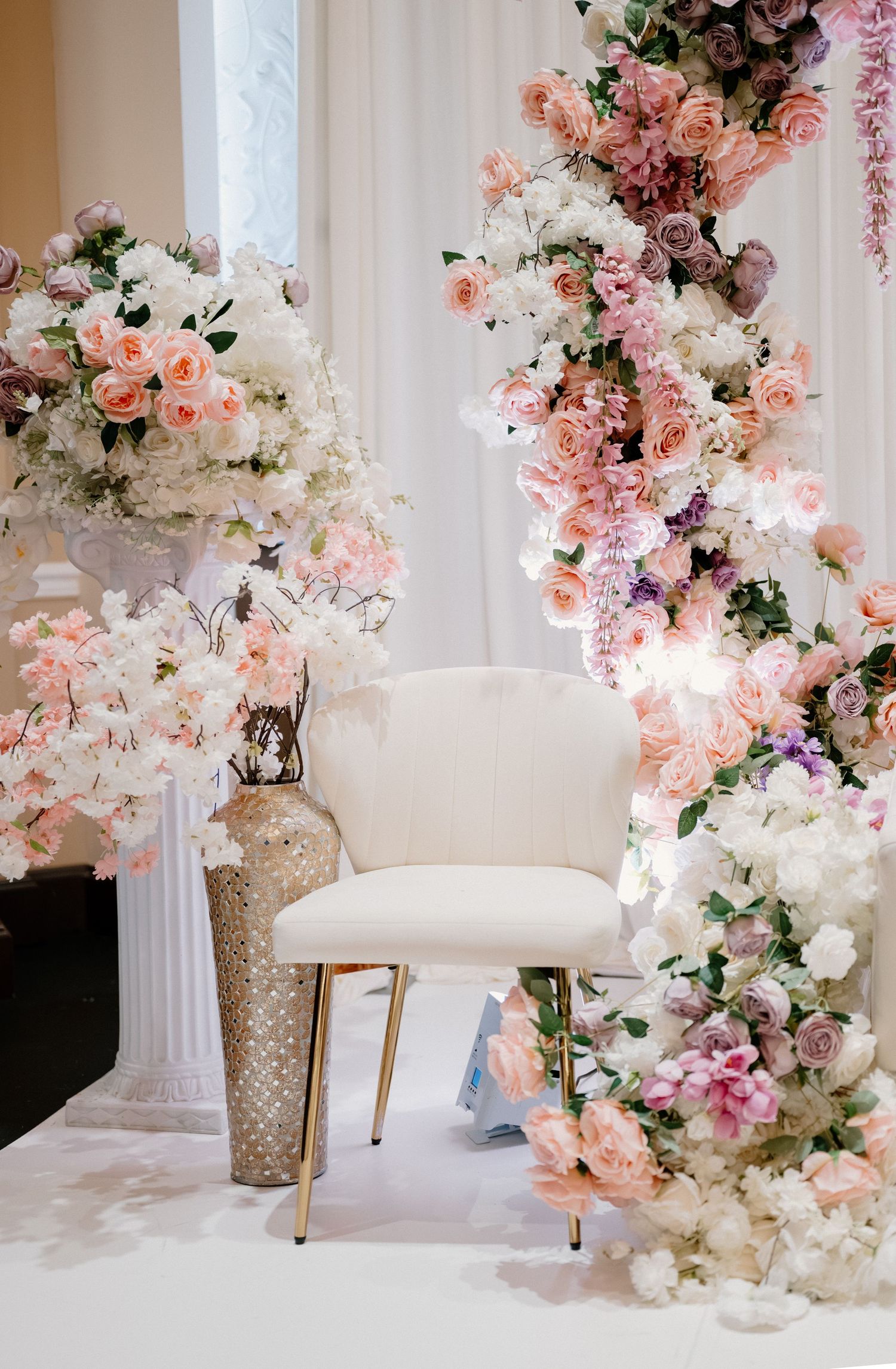 Luxurious wedding backdrop with pink and white roses cascading over elegant white chairs.