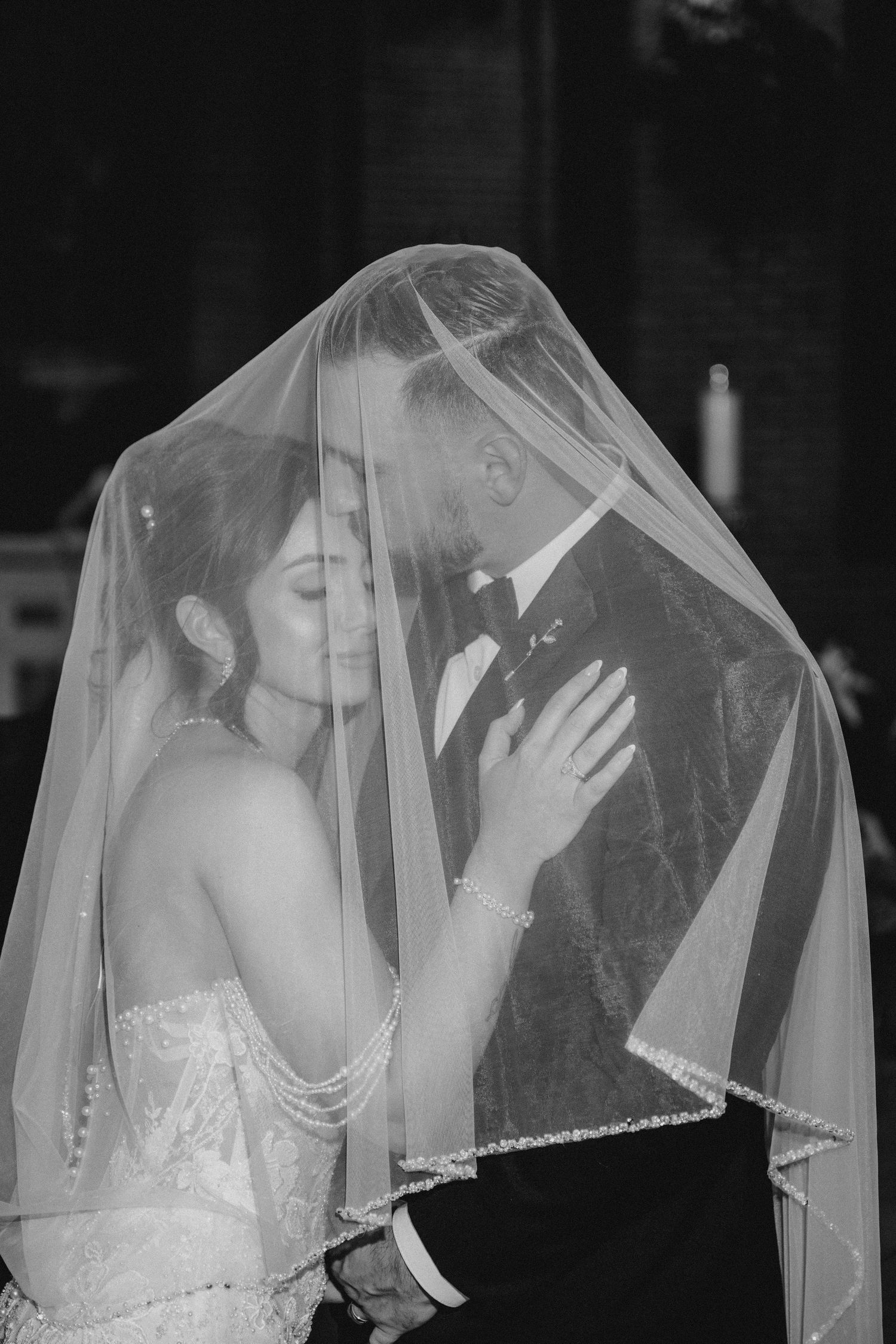 Black and white photo of bride and groom sharing intimate moment under wedding veil.