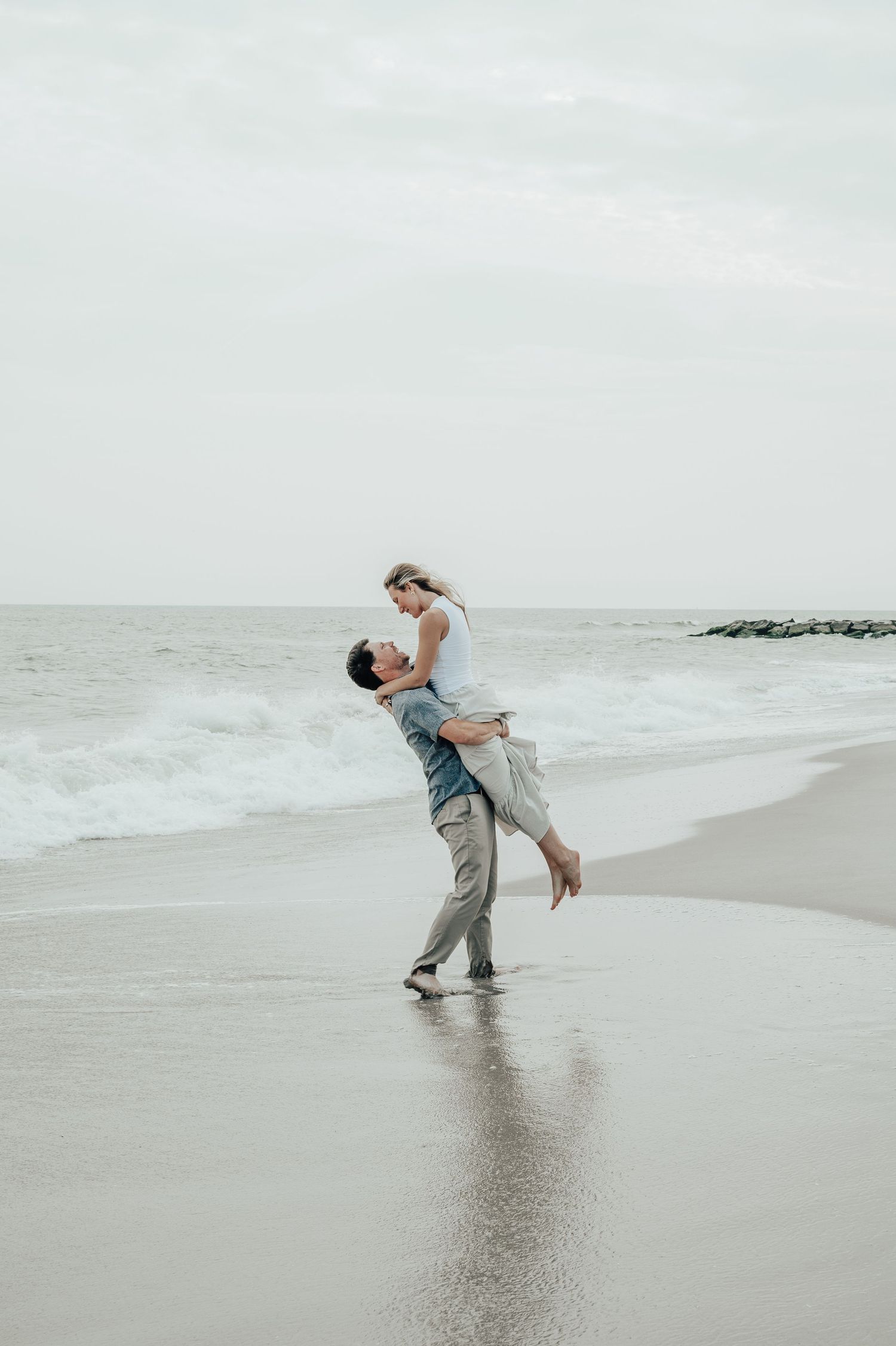 A joyful moment captured on a misty beach as a couple embraces.