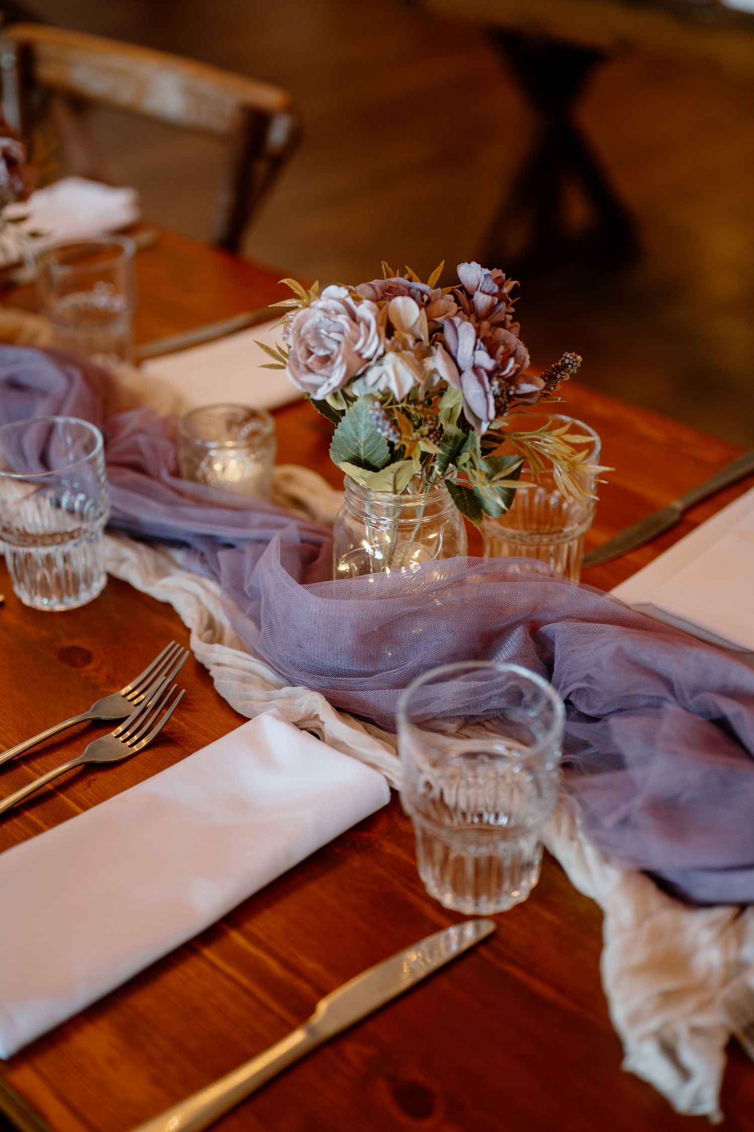 Elegant table setting with purple linens, crystal glasses and floral centerpieces on wooden surface.