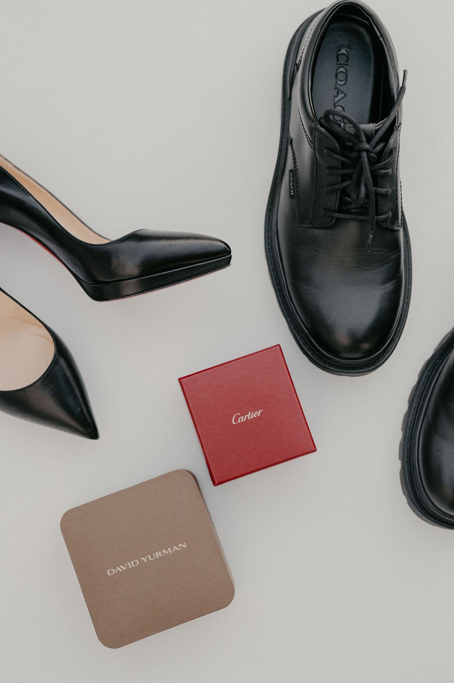 Luxury fashion flatlay with black leather shoes and designer brand cards from Cartier and David Yurman on white background.