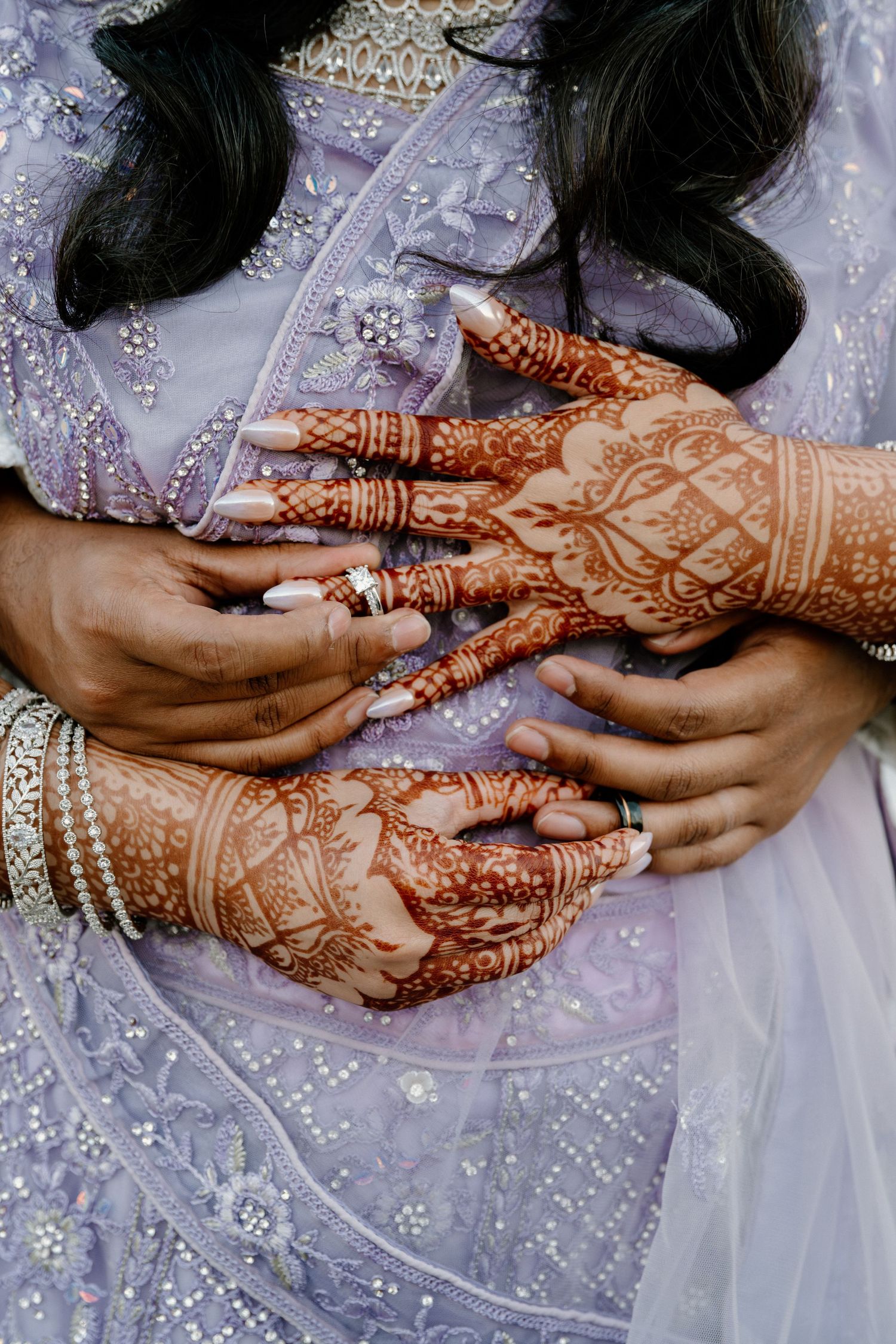 Detailed henna designs on hands with wedding rings and sparkly fabric.