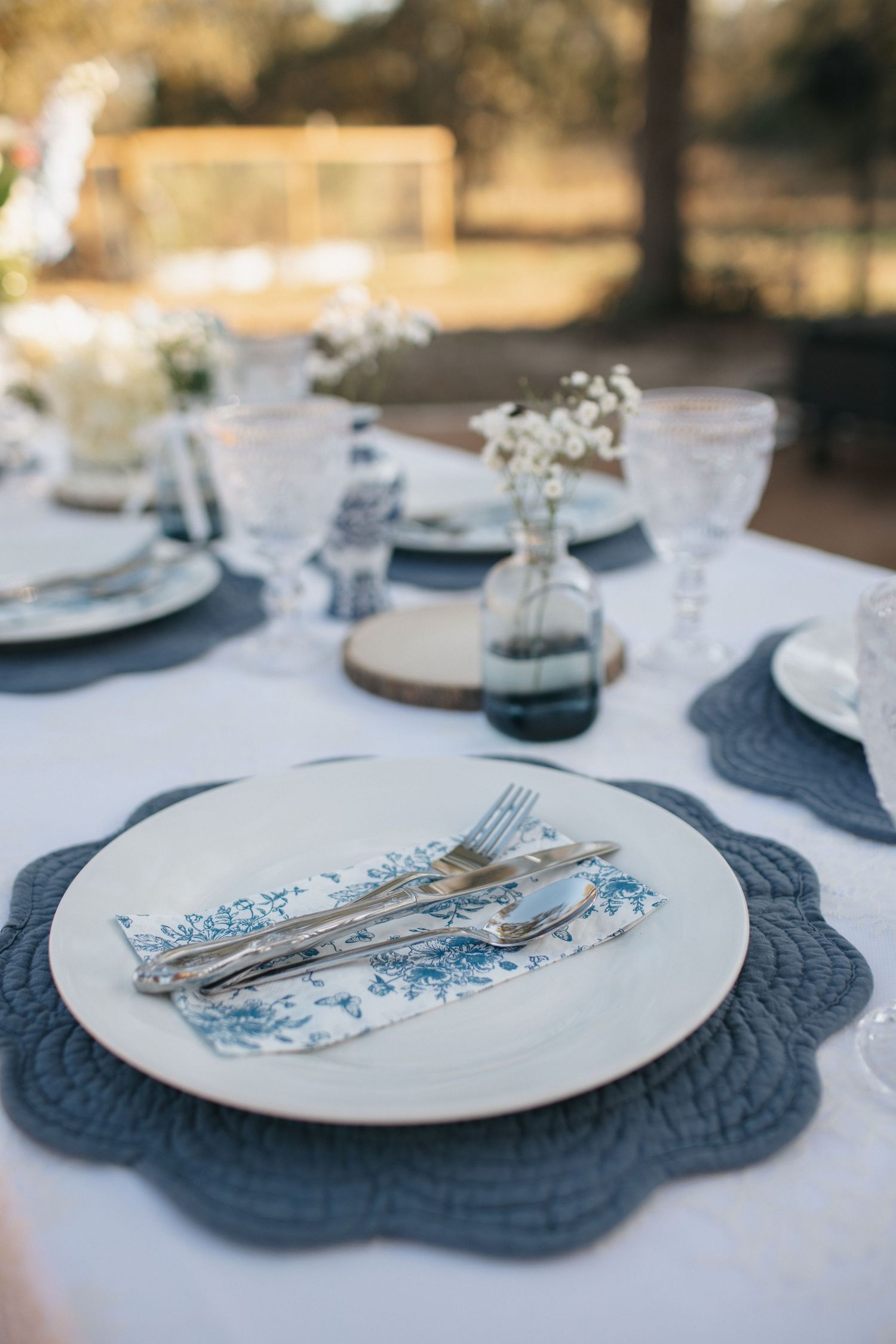 Elegant place setting with white plates and navy blue chargers on a rustic wooden table.