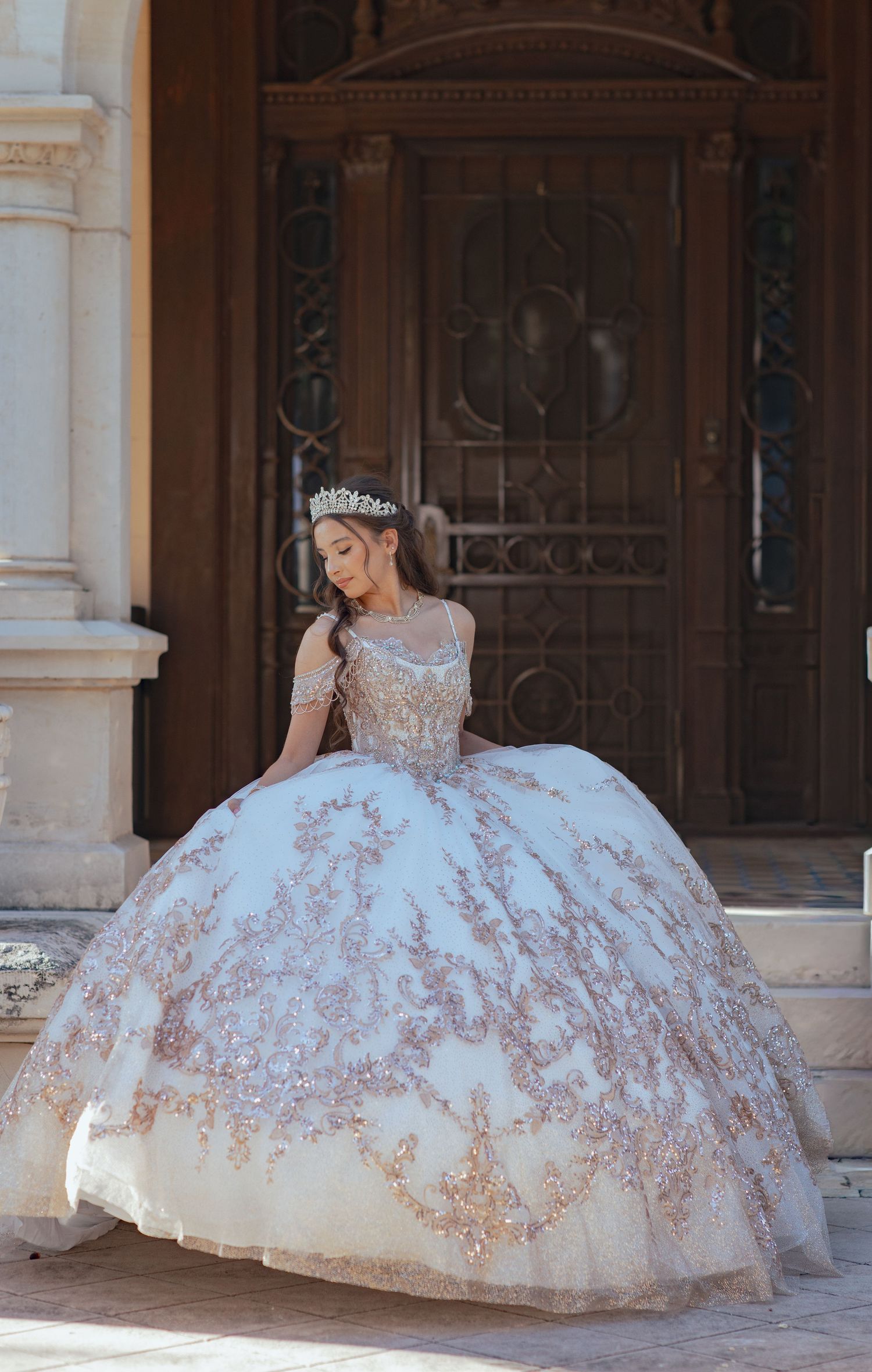 Ornate white and gold ballgown with detailed embroidery captured under architectural arches.