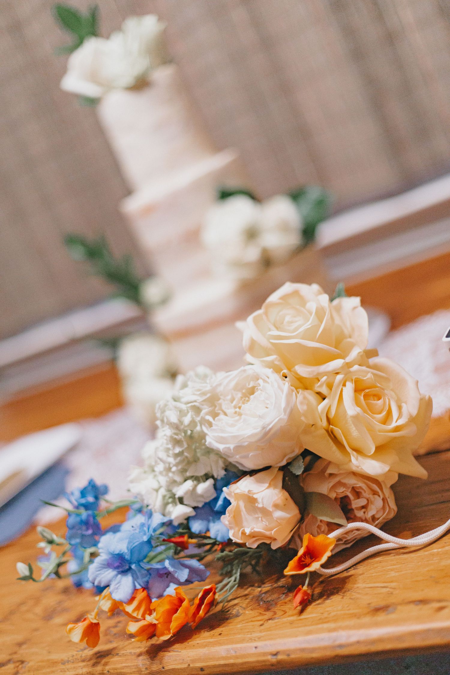 Wedding bouquet with peach roses and blue delphinium arranged on wooden surface.