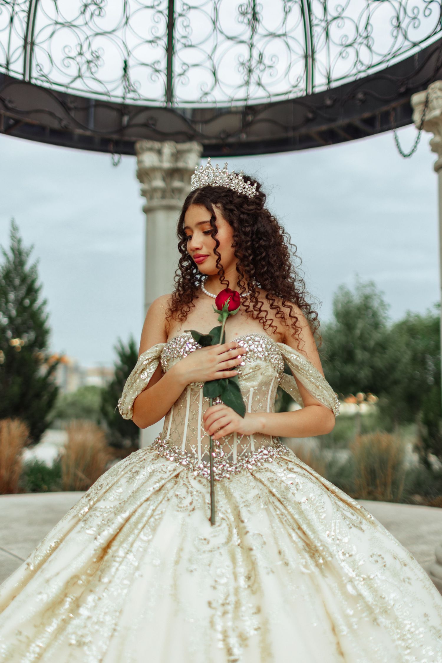 An elegant ball gown photoshoot under a decorative metal gazebo with white columns.