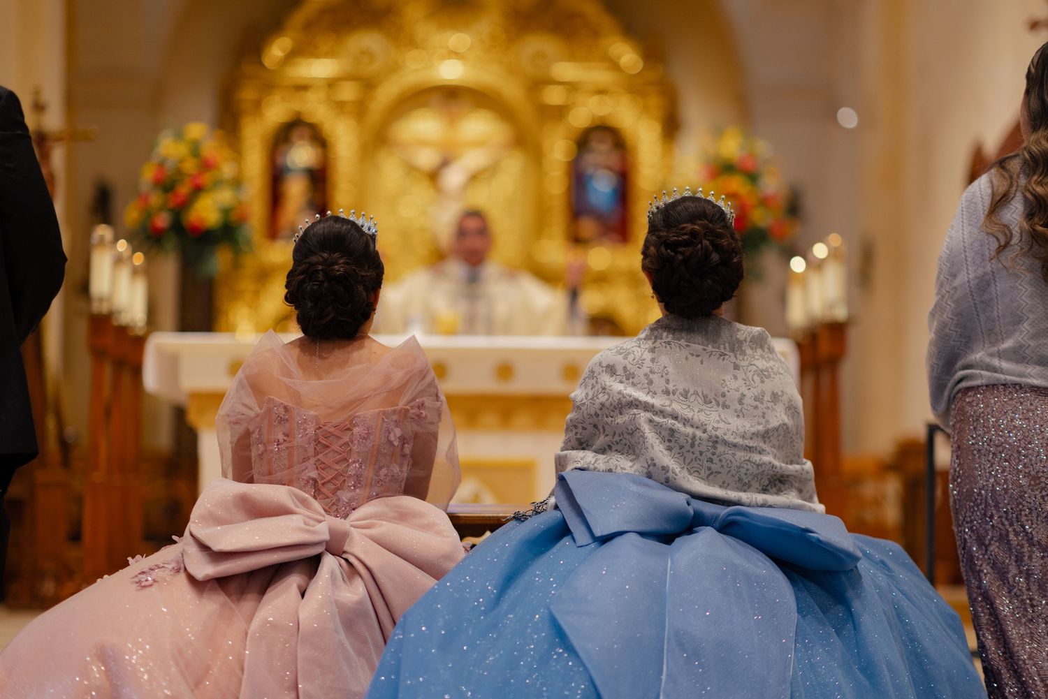 Back view of formal dresses with oversized bows during church ceremony with golden altar in background.