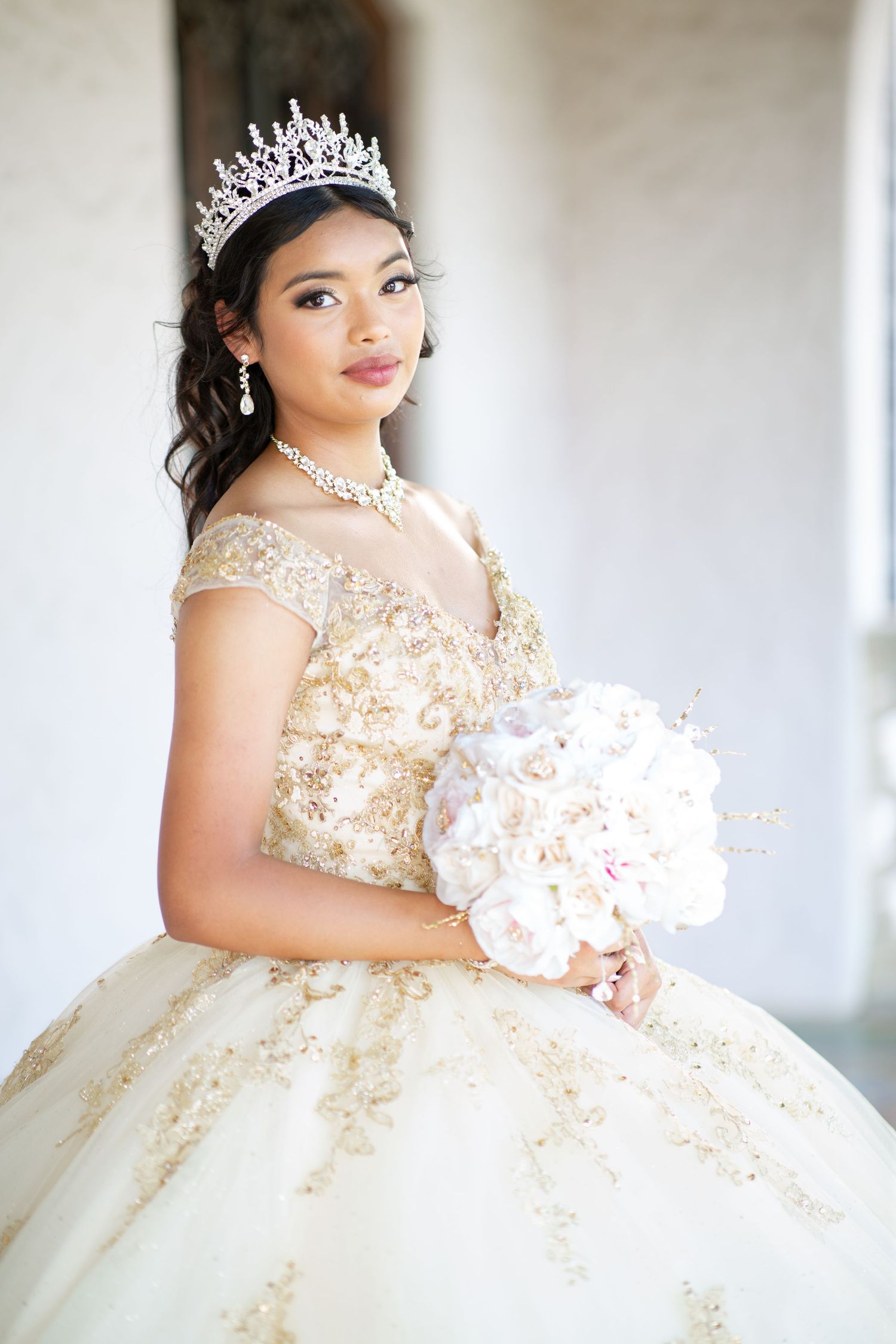 Elegant portrait featuring cream ballgown with gold details and pink floral bouquet.