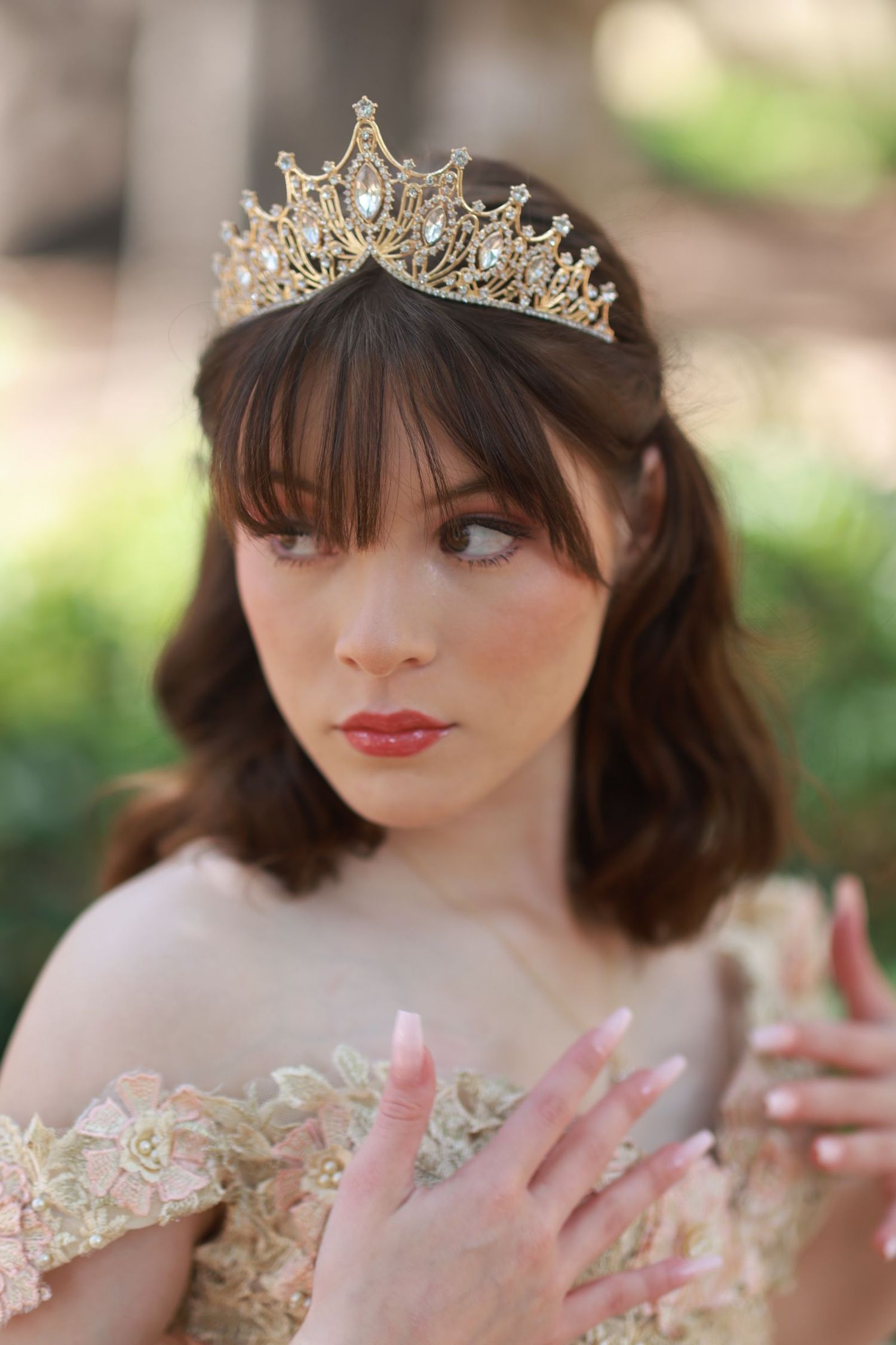Close-up portrait wearing a sparkling tiara and pink lipstick against a blurred natural background.