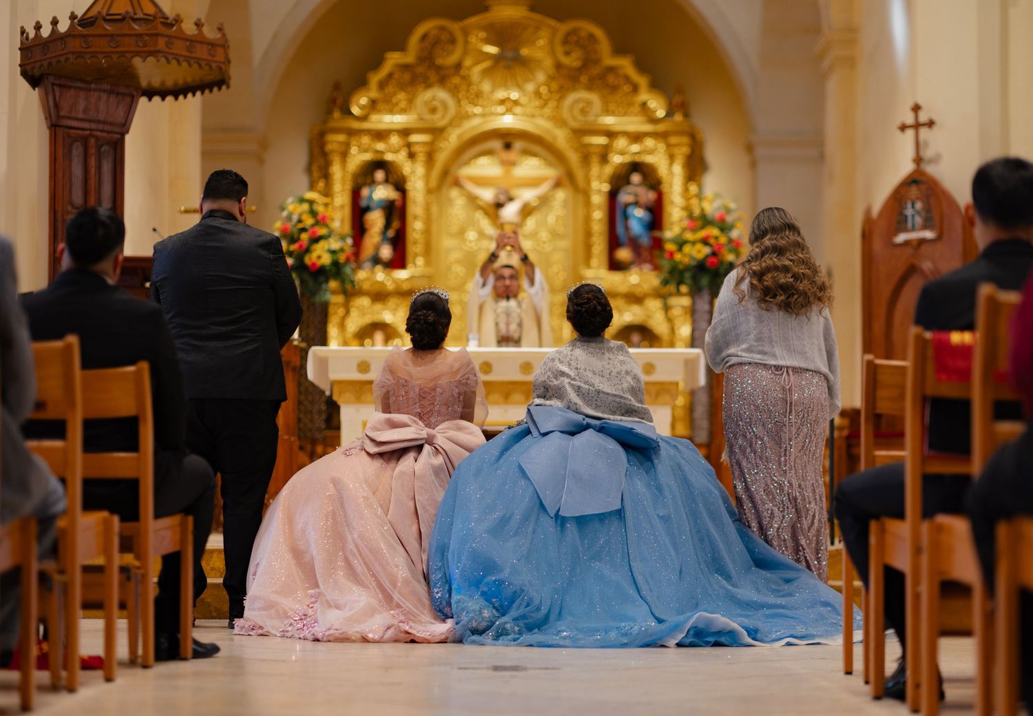 View from behind of formal ceremony in Catholic church with golden altar and decorative arches.
