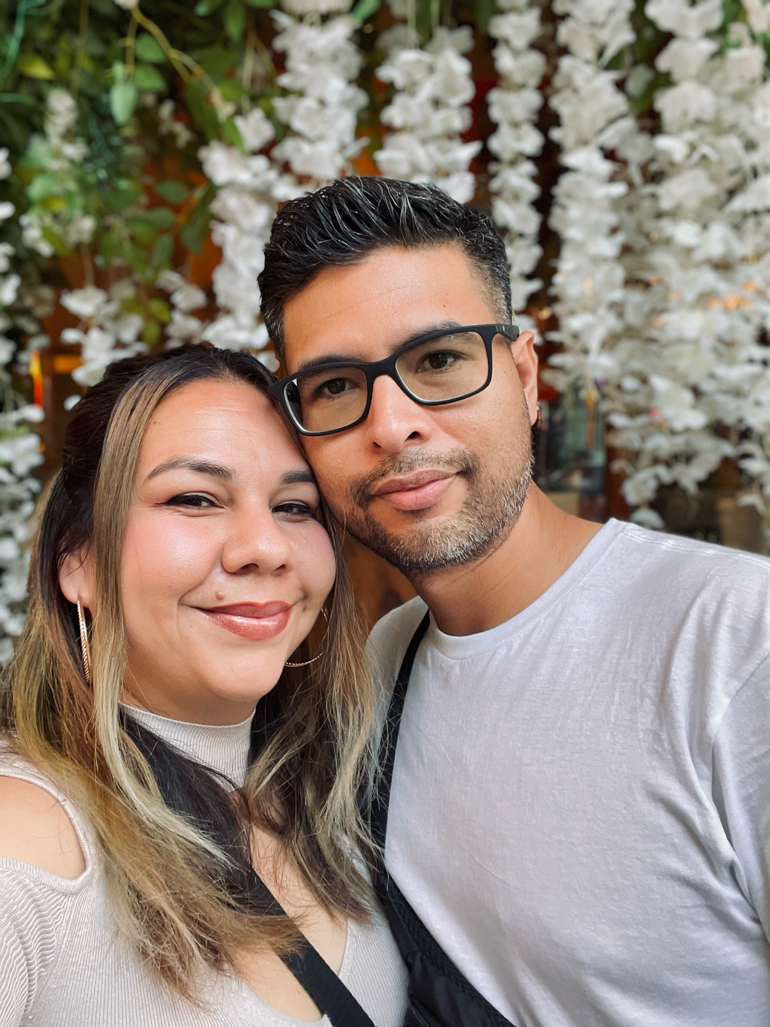 Couple takes selfies in front of decorative white floral backdrop.