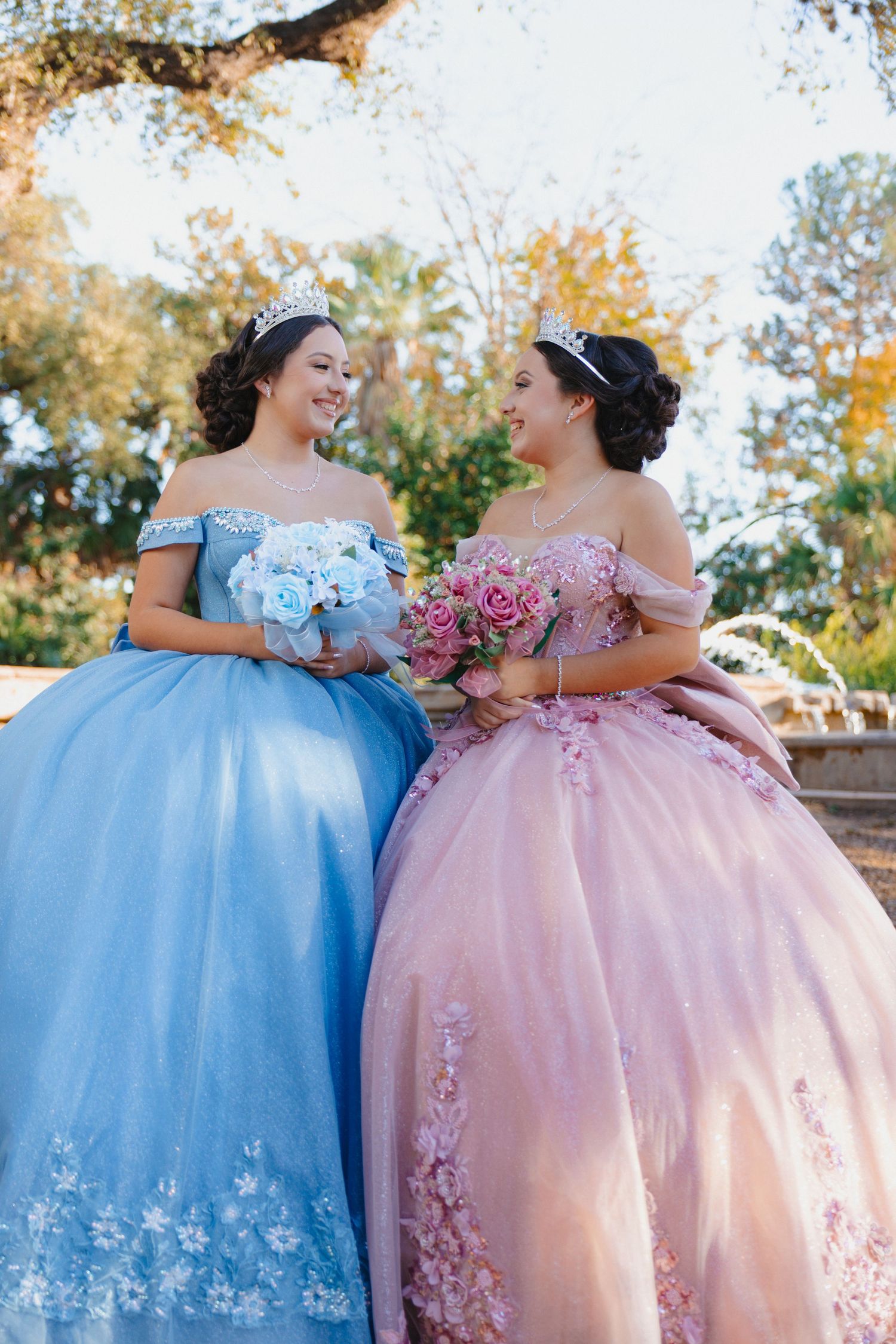 Two elegant ballgowns in baby blue and pink photographed outdoors.