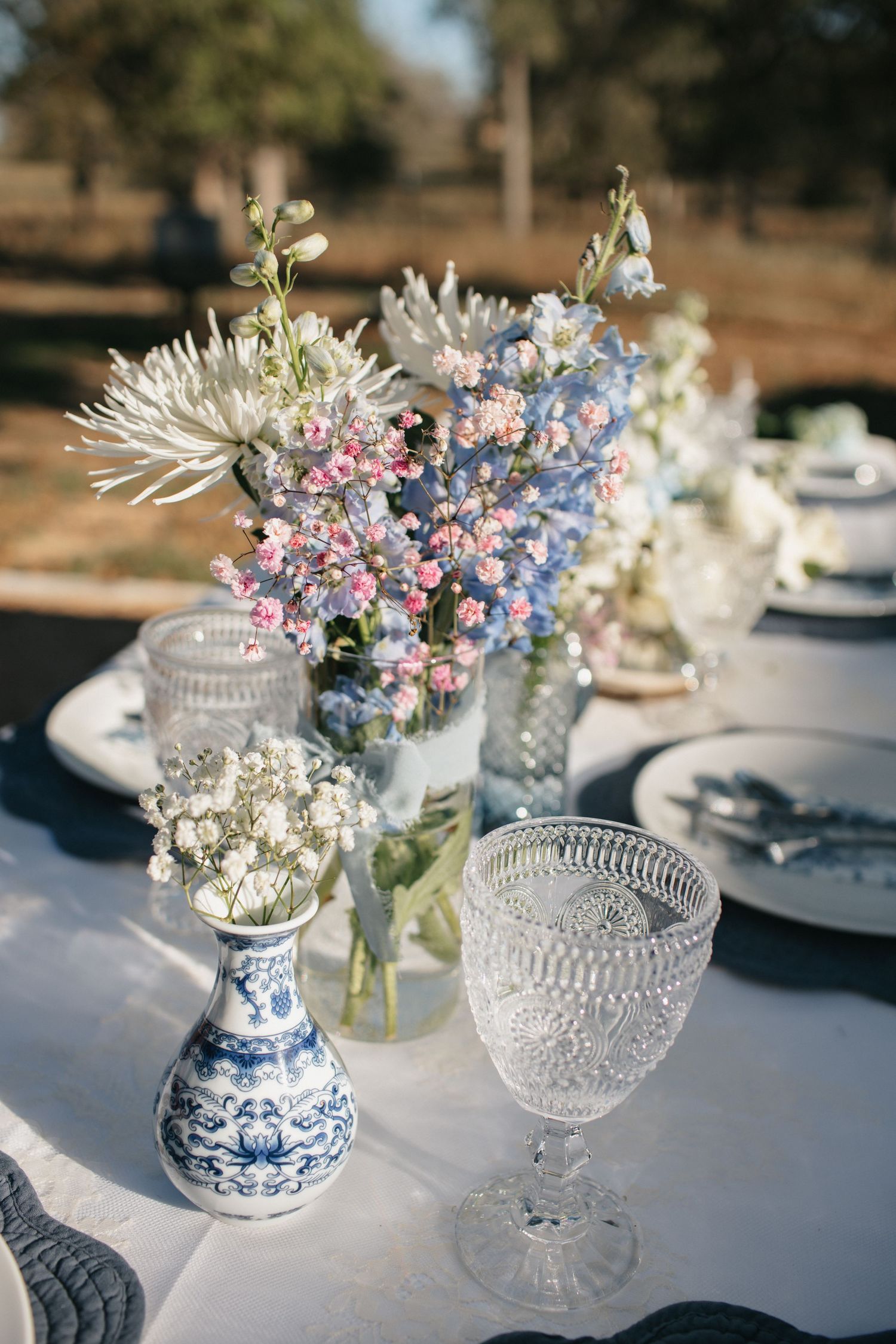 Romantic table centerpieces featuring blue and pink flowers in vintage crystal vases.
