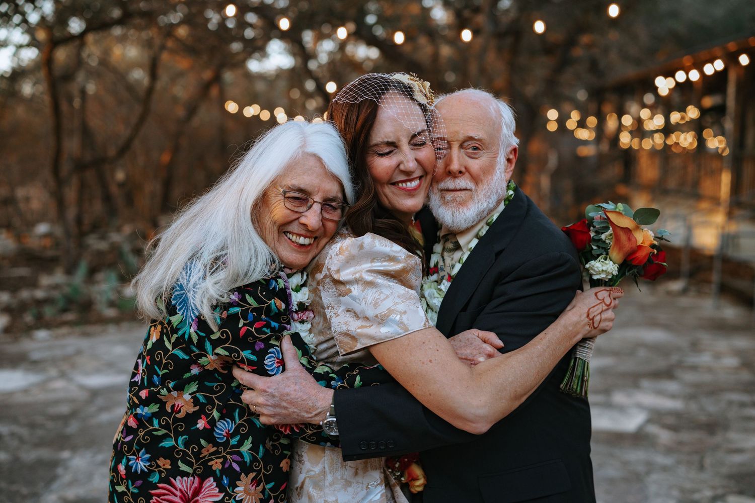 Joyful wedding celebration with string lights and autumn foliage in background.