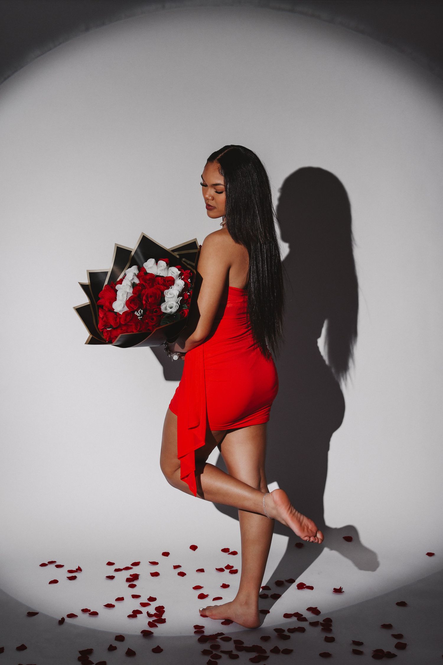 Dynamic fashion shoot with red dress and rose bouquet against stark white spotlight.