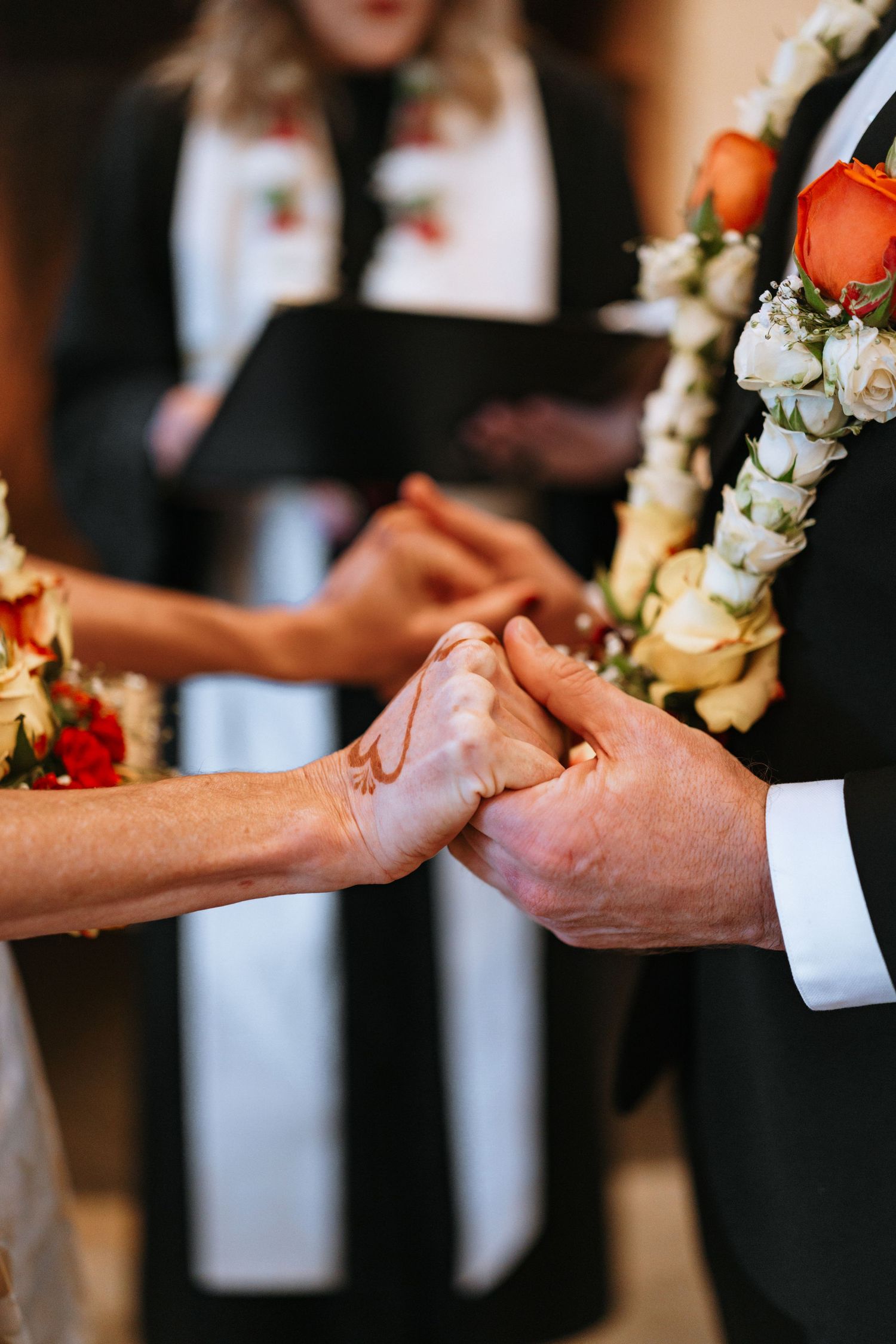 Close-up of hands joining together during wedding ceremony with floral backdrop.
