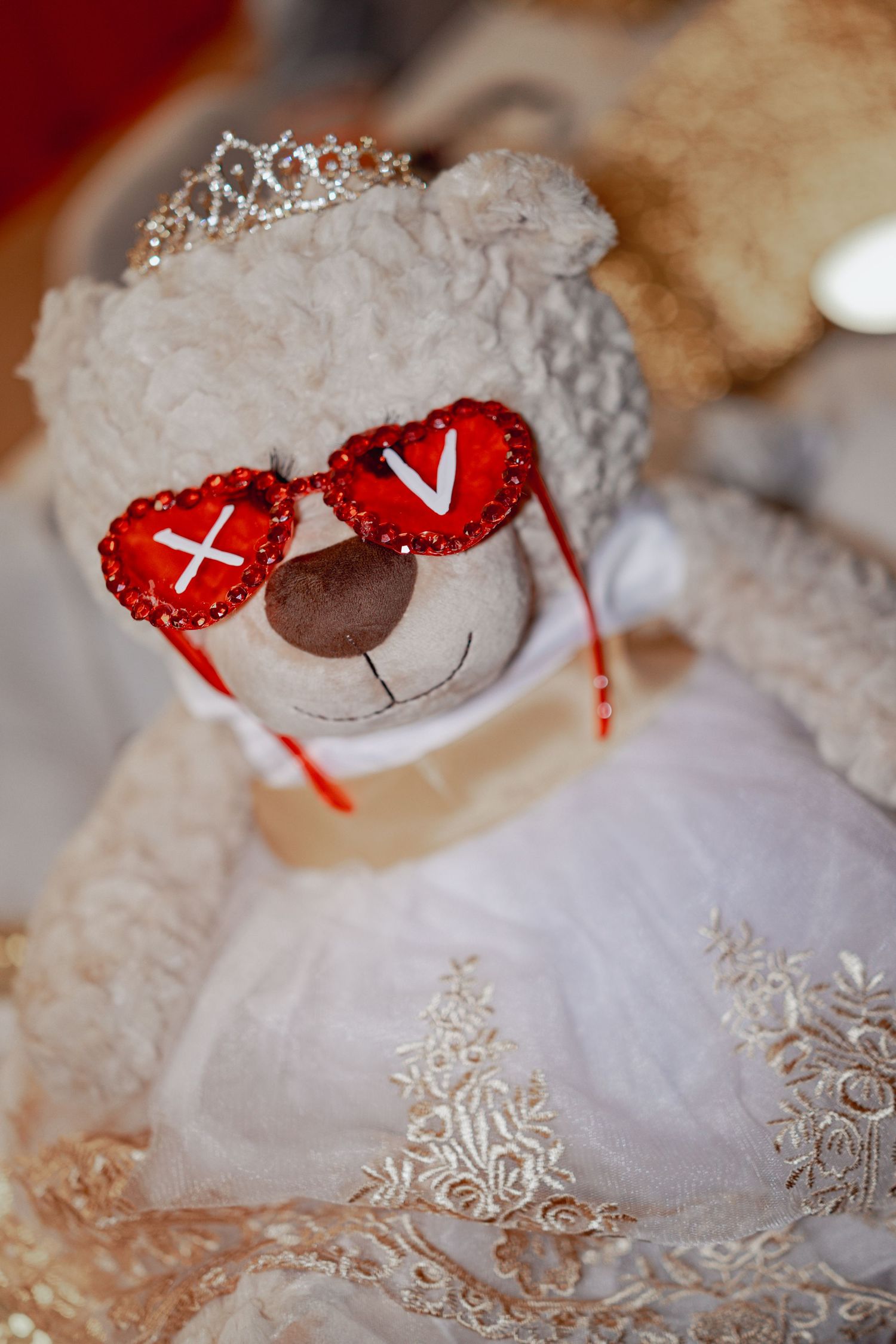 A decorative white dress with intricate embroidery details and a plush teddy bear wearing red accessories.