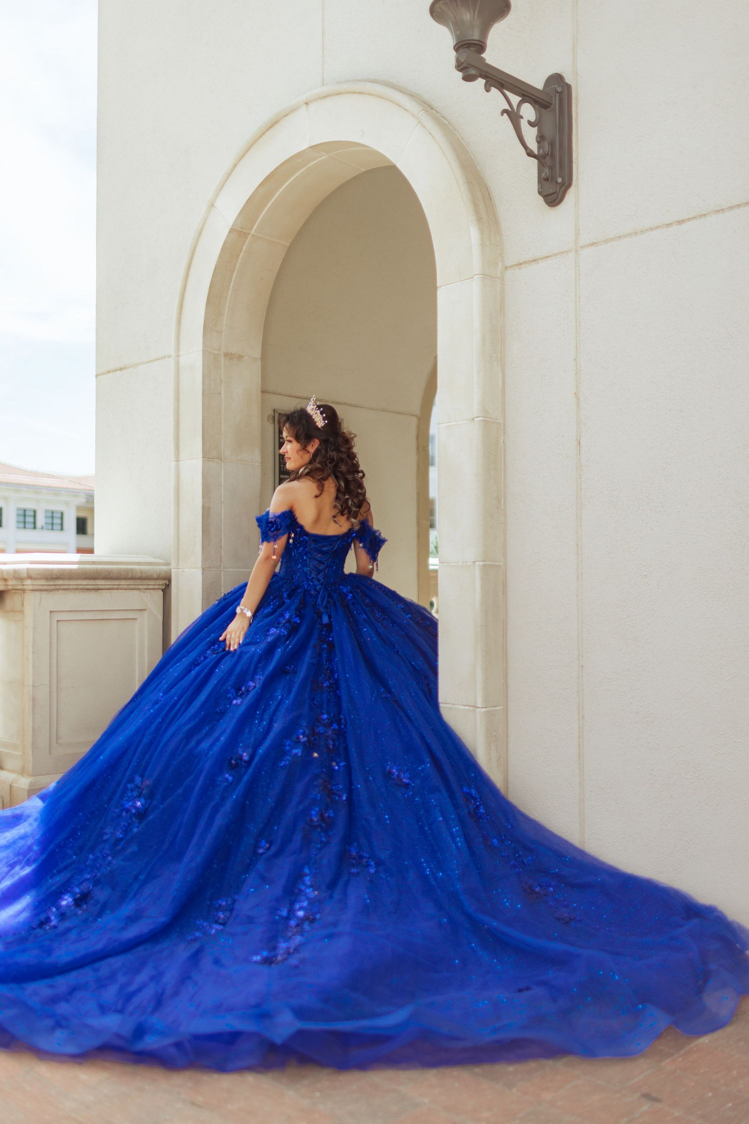 Dramatic royal blue ballgown with long train photographed under white archways.