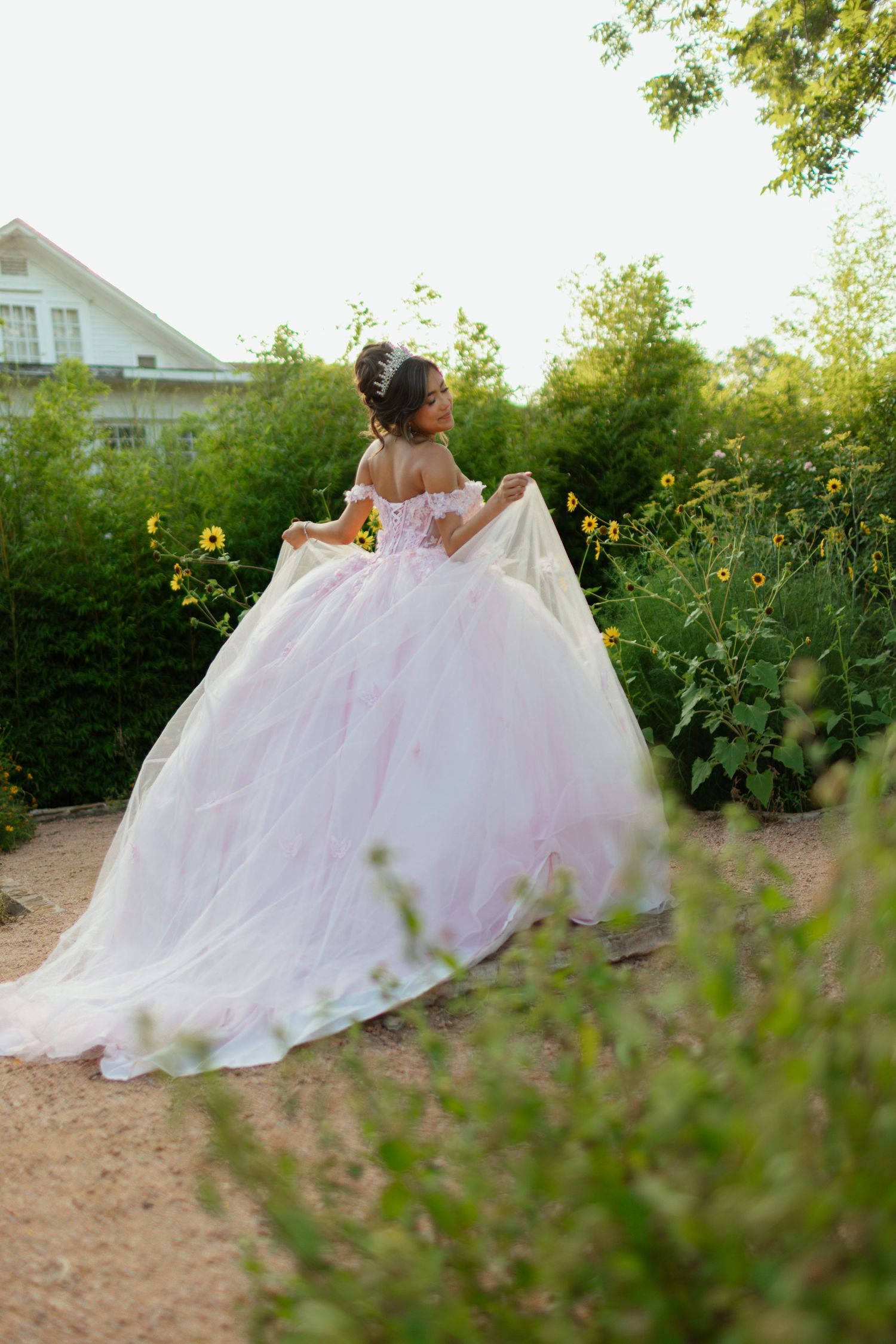 Sweeping garden shot of a voluminous white ballgown against summer foliage.