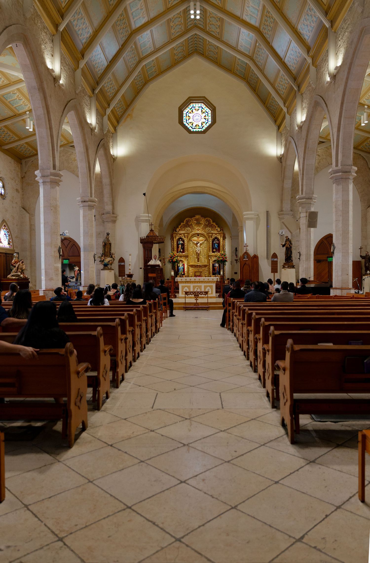 Interior of Catholic church with vaulted ceiling, wooden pews, and ornate altar at the end of center aisle.
