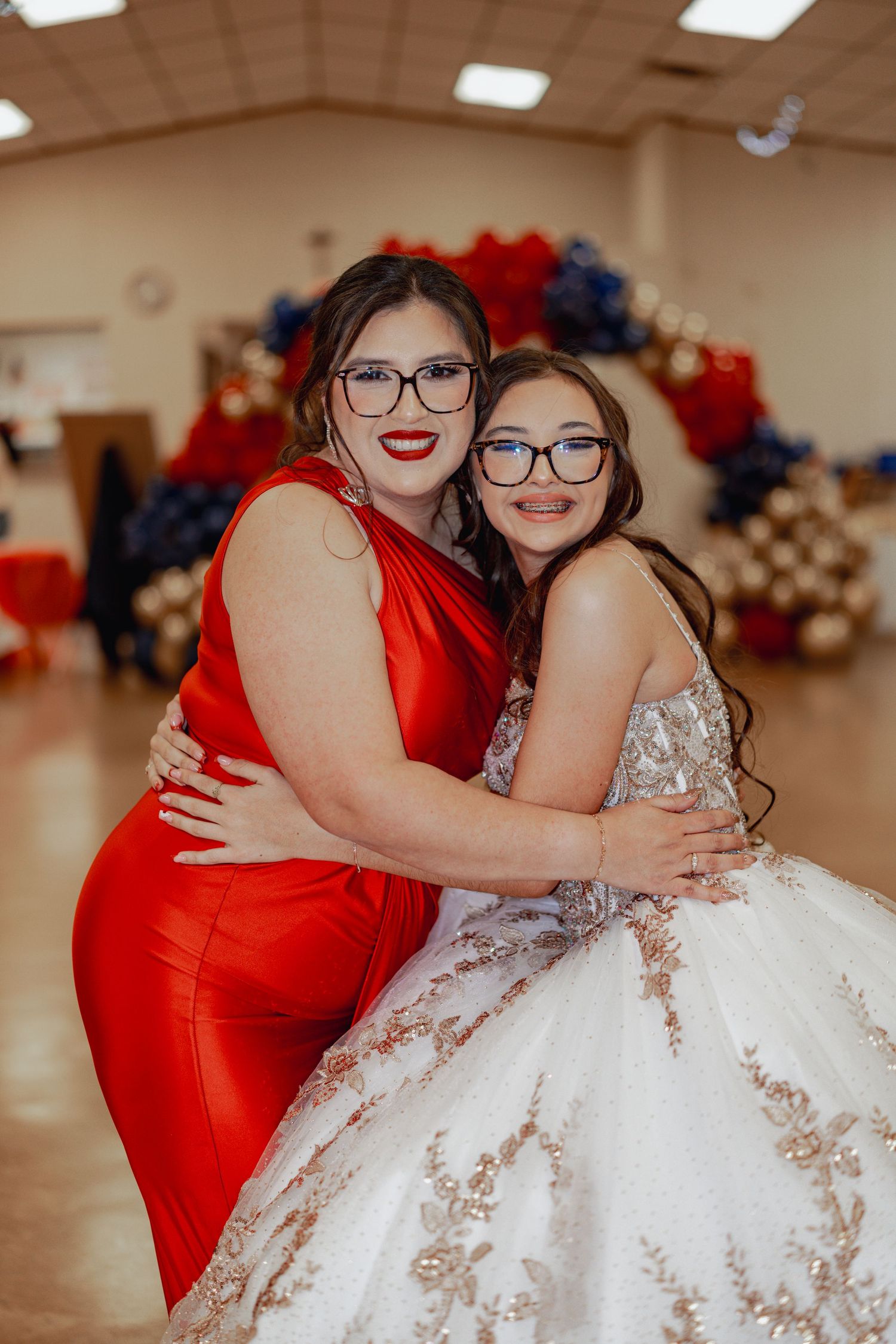 Celebration scene with red formal dress and white ball gown in decorated hall.