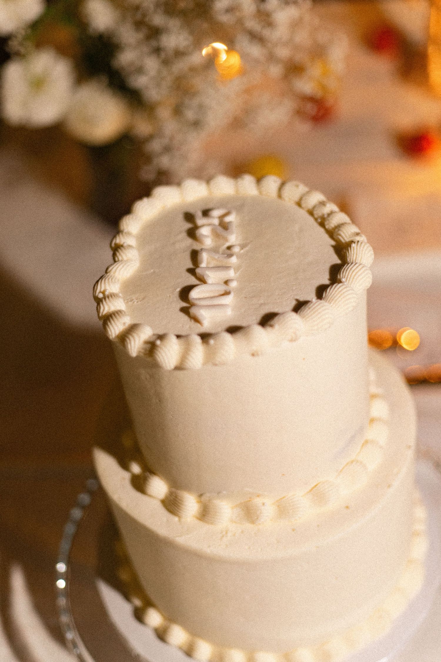 A classic white tiered wedding cake with simple piped decorations displayed at a reception.