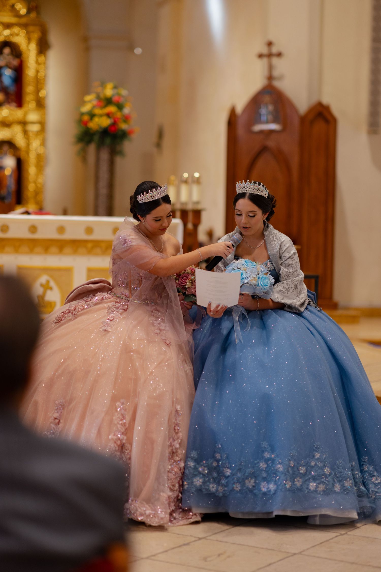 Two formal gowns in pink and blue share a moment in a church setting.