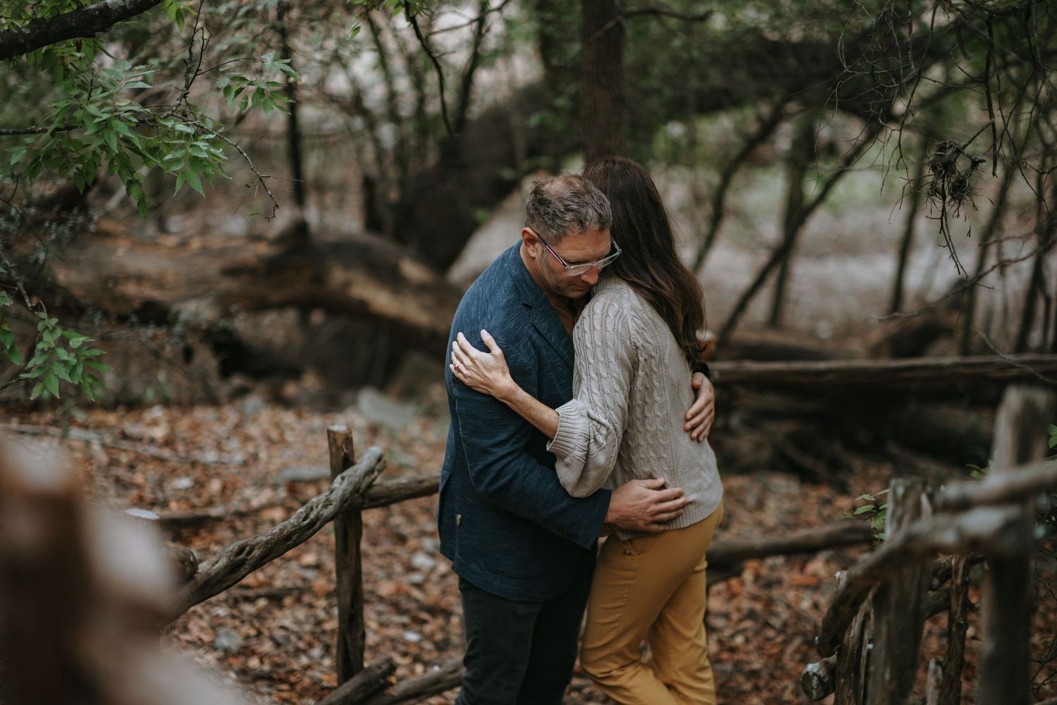 Intimate engagement photo of couple embracing on wooden bridge in autumn forest.
