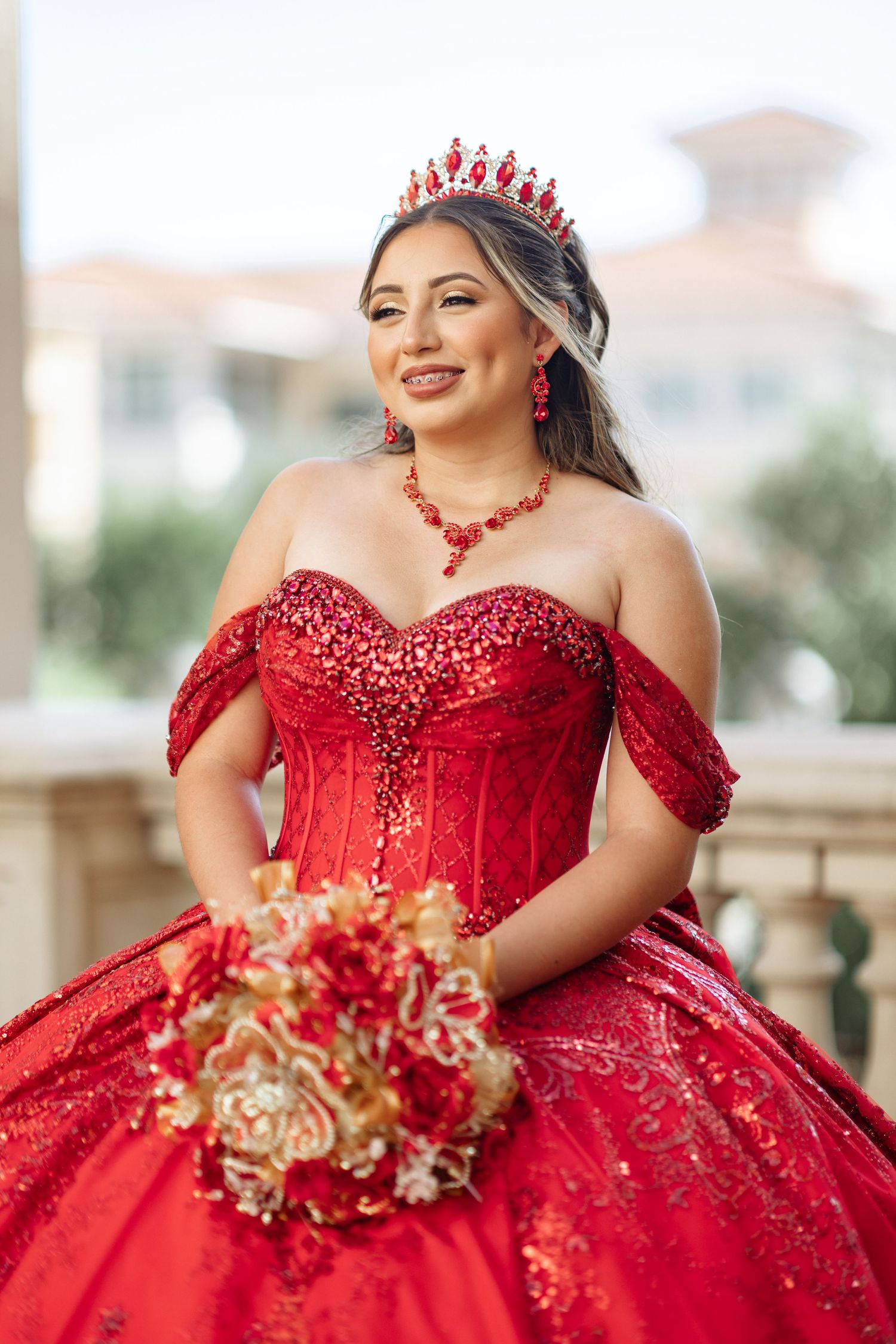 A stunning red ball gown with matching crown and floral bouquet photographed outdoors.