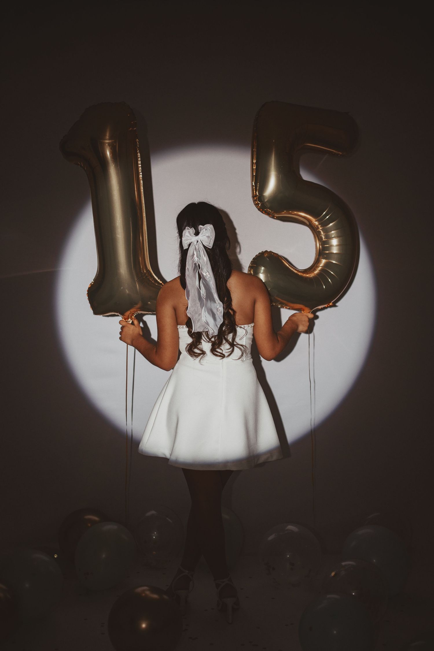 Artistic portrait with large gold number 15 balloons and dramatic spotlight effect.