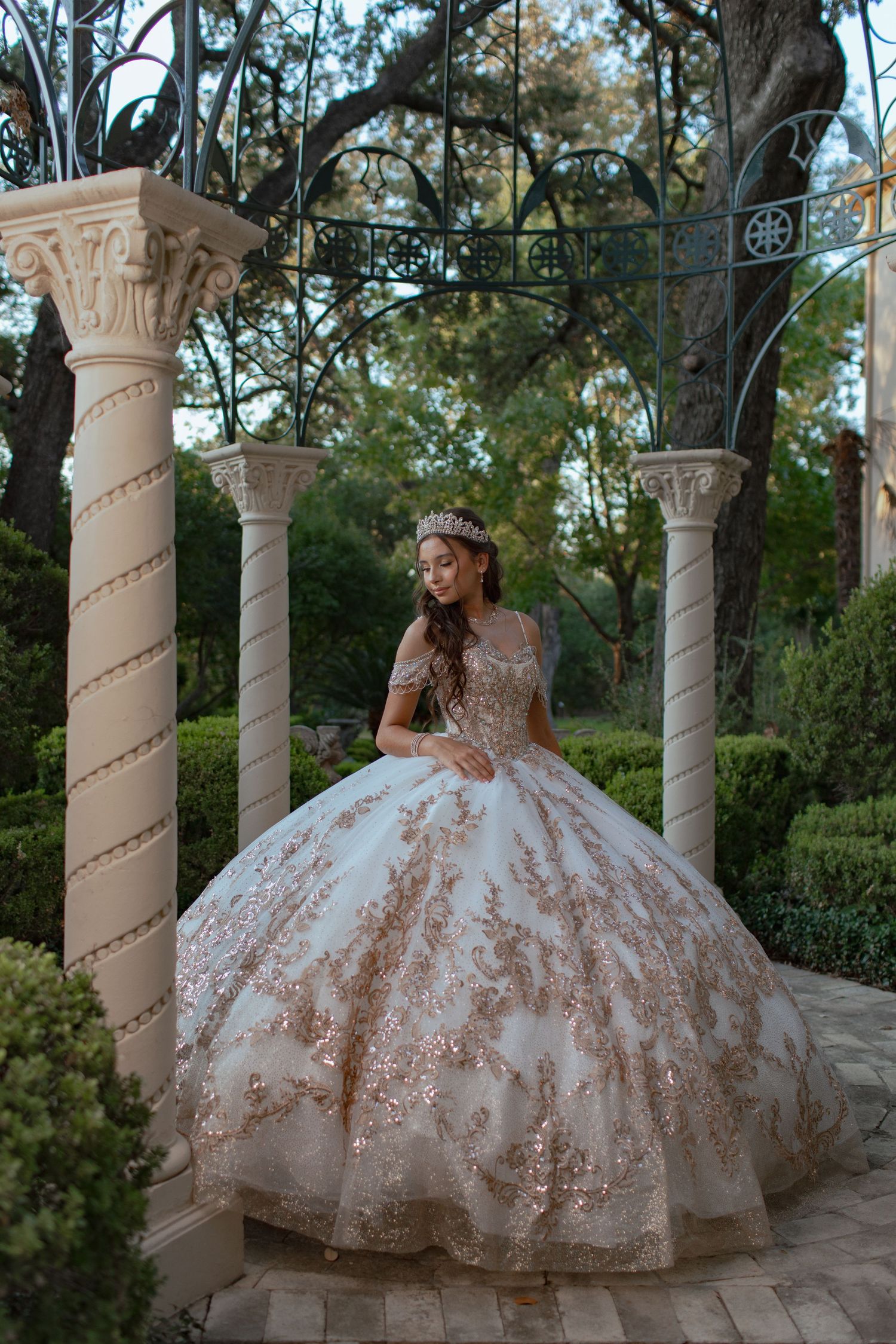 Ornate quinceanera dress with sparkly details photographed in an elegant outdoor colonnade setting.