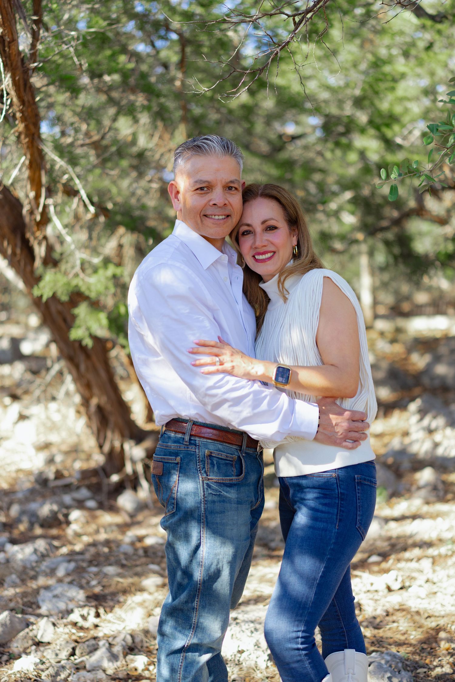 Casual couple portrait in white shirts and jeans against natural outdoor setting.