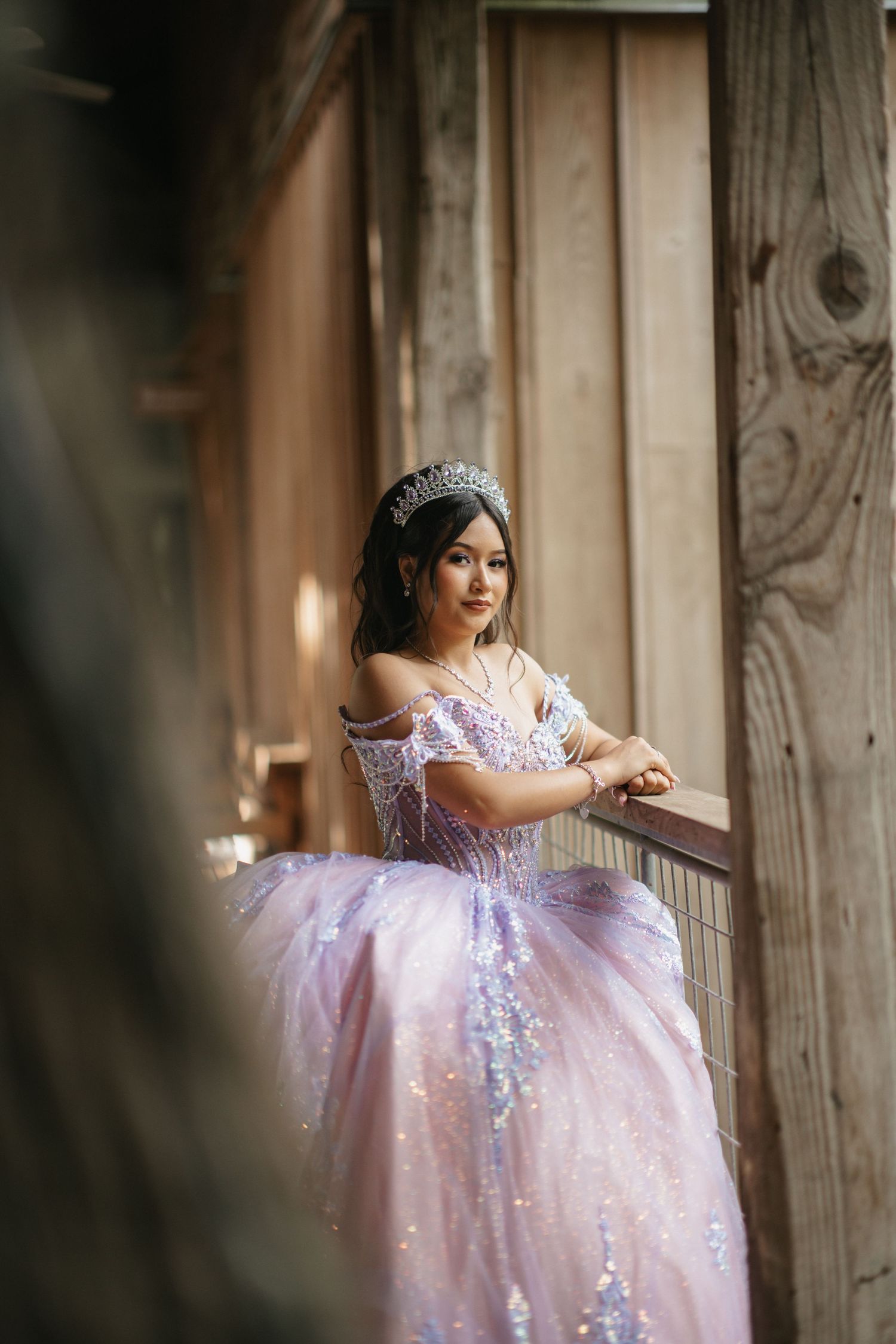 A dreamy portrait of a ballgown with sparkly details near a rustic wooden railing.