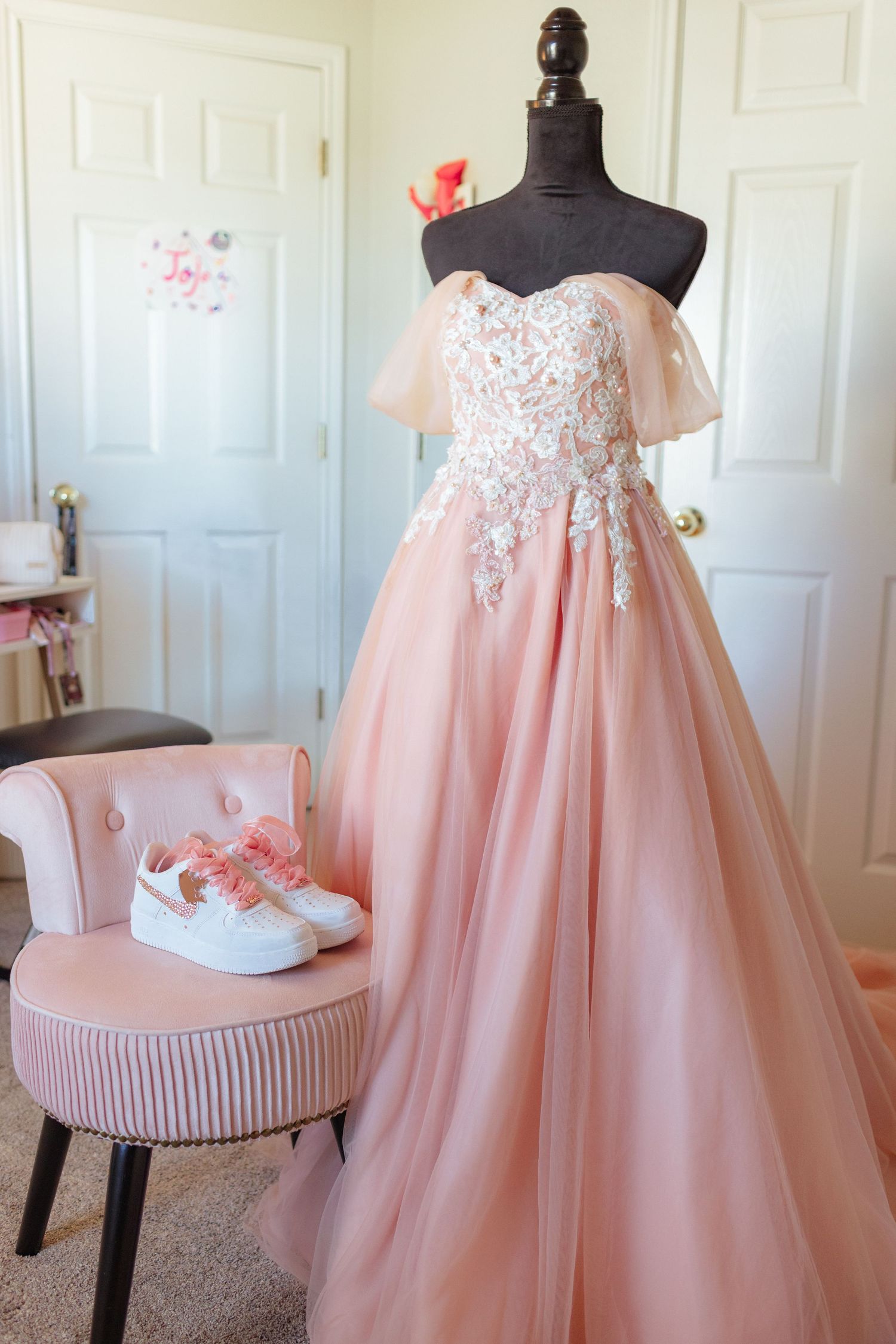 Blush pink formal gown with white lace appliques displayed on a dress form.