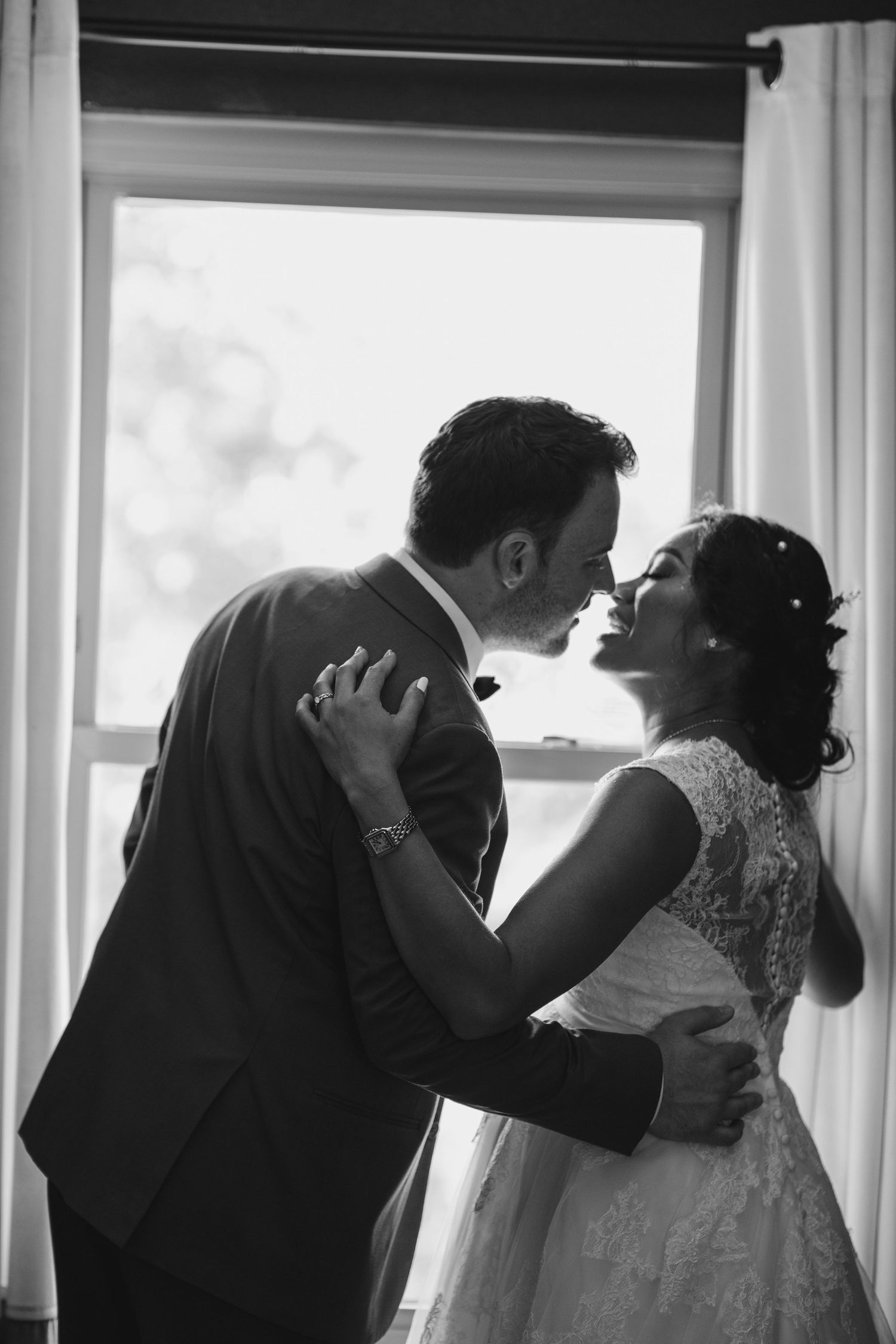 Romantic black and white wedding photo of couple embracing by window.
