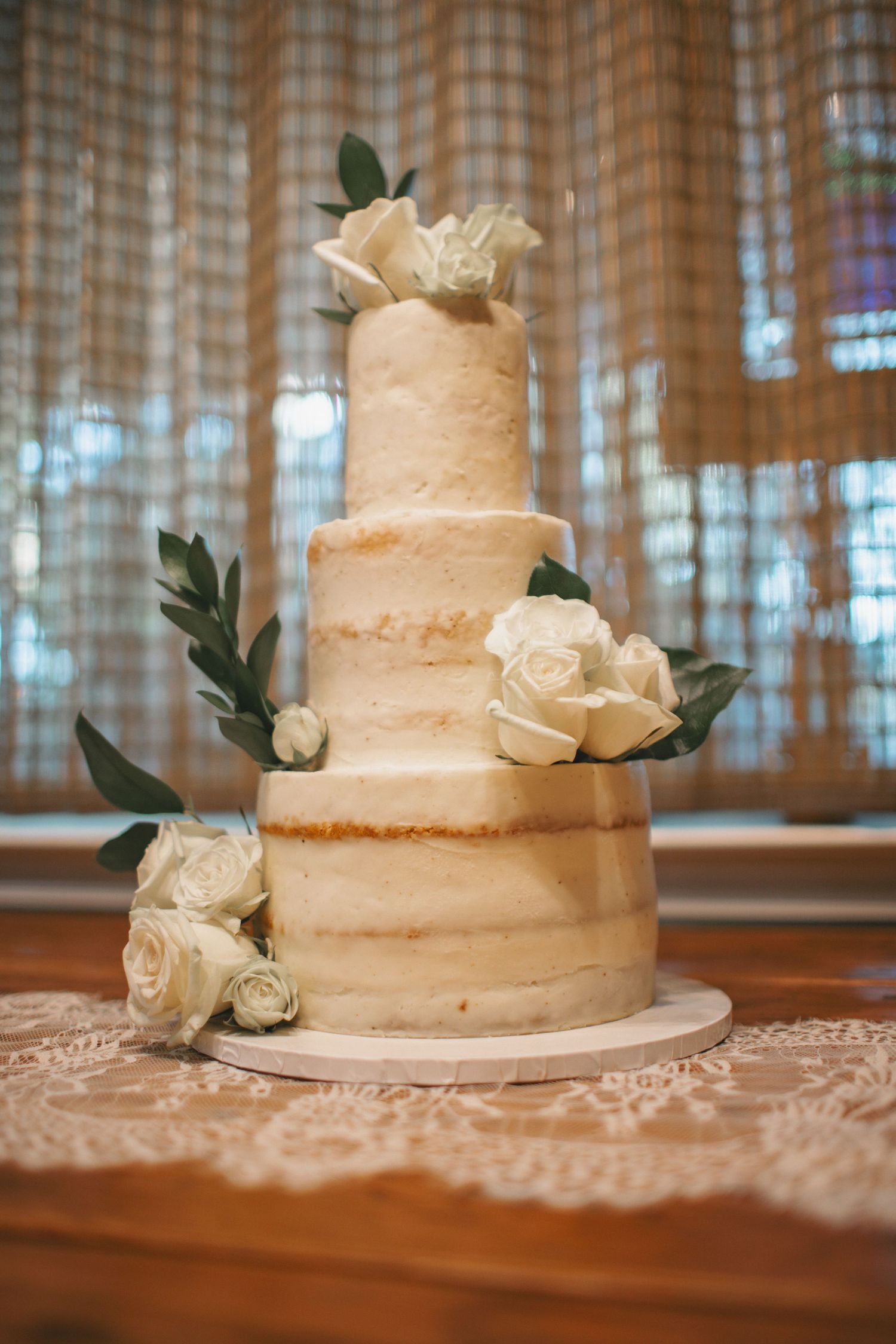 Elegant three-tier white wedding cake decorated with fresh roses and greenery.