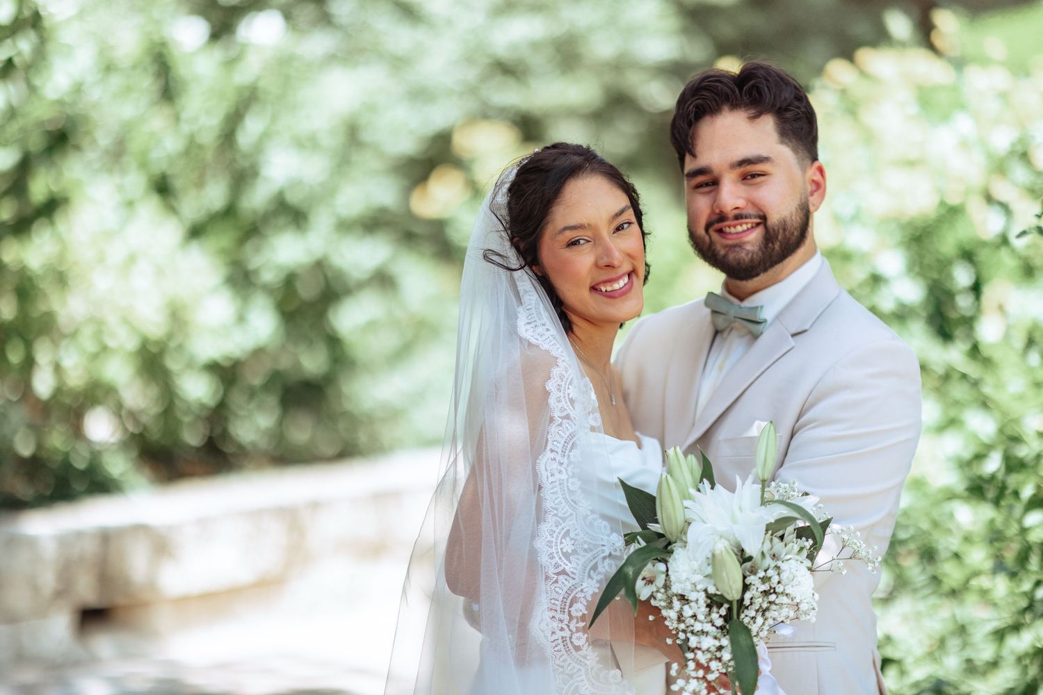 Newlyweds sharing joyful moments in a lush garden setting with white floral bouquet.