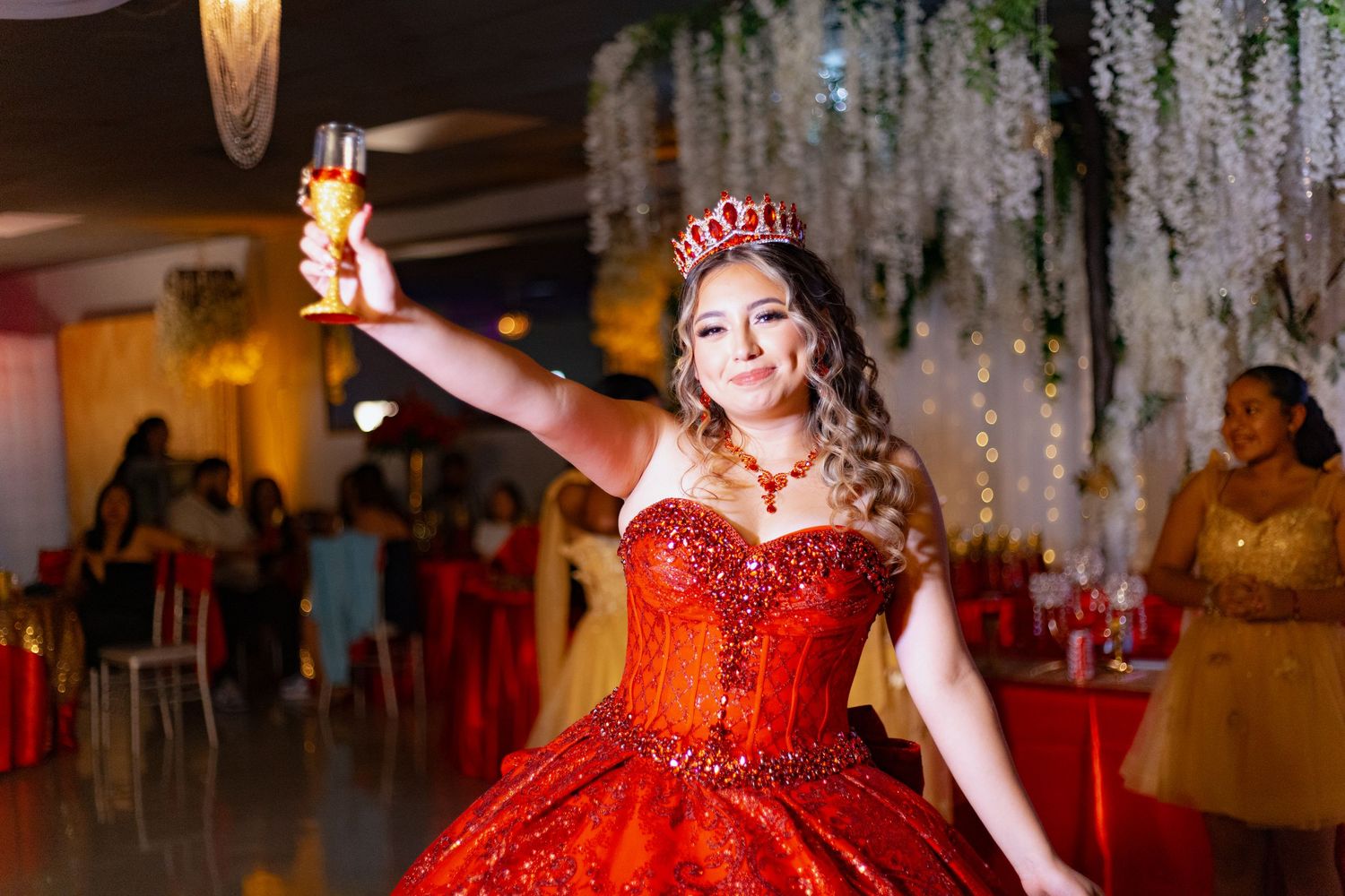A celebrant in a sparkling red gown raises a toast during a festive party.