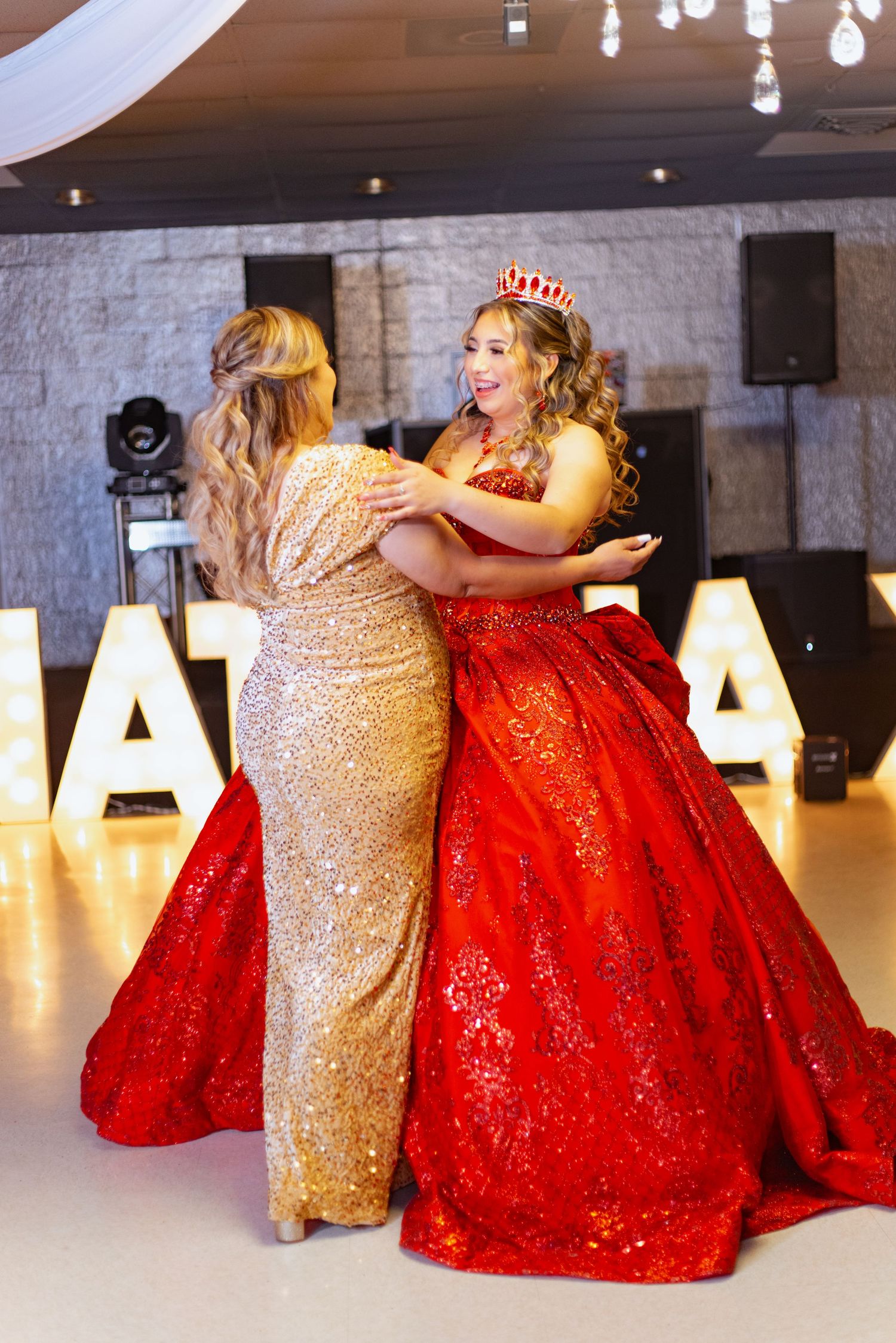 Two people in formal attire sharing a celebratory moment in front of illuminated letters.