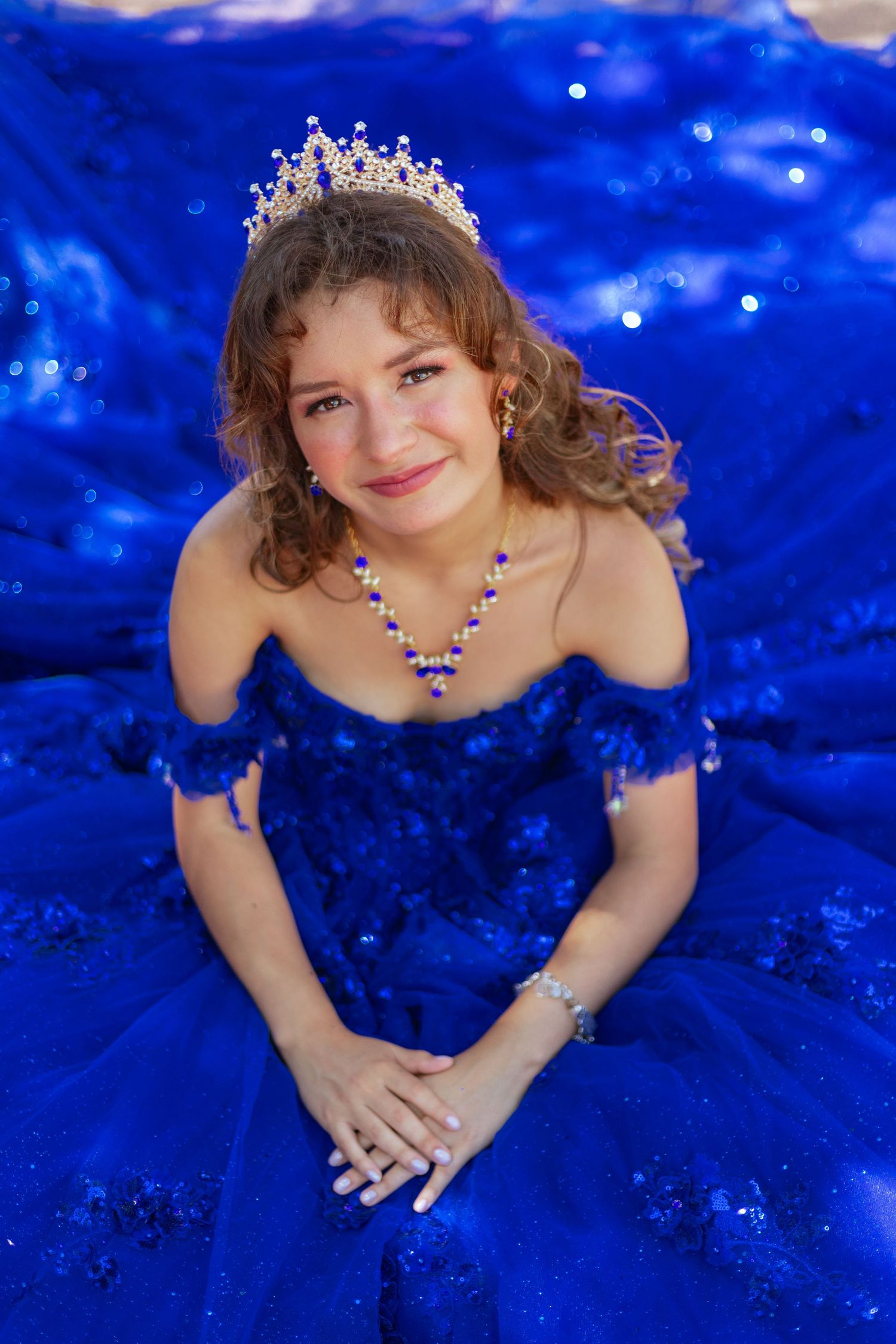Elegant royal blue ball gown with sparkly details and tiara against a vibrant blue backdrop.