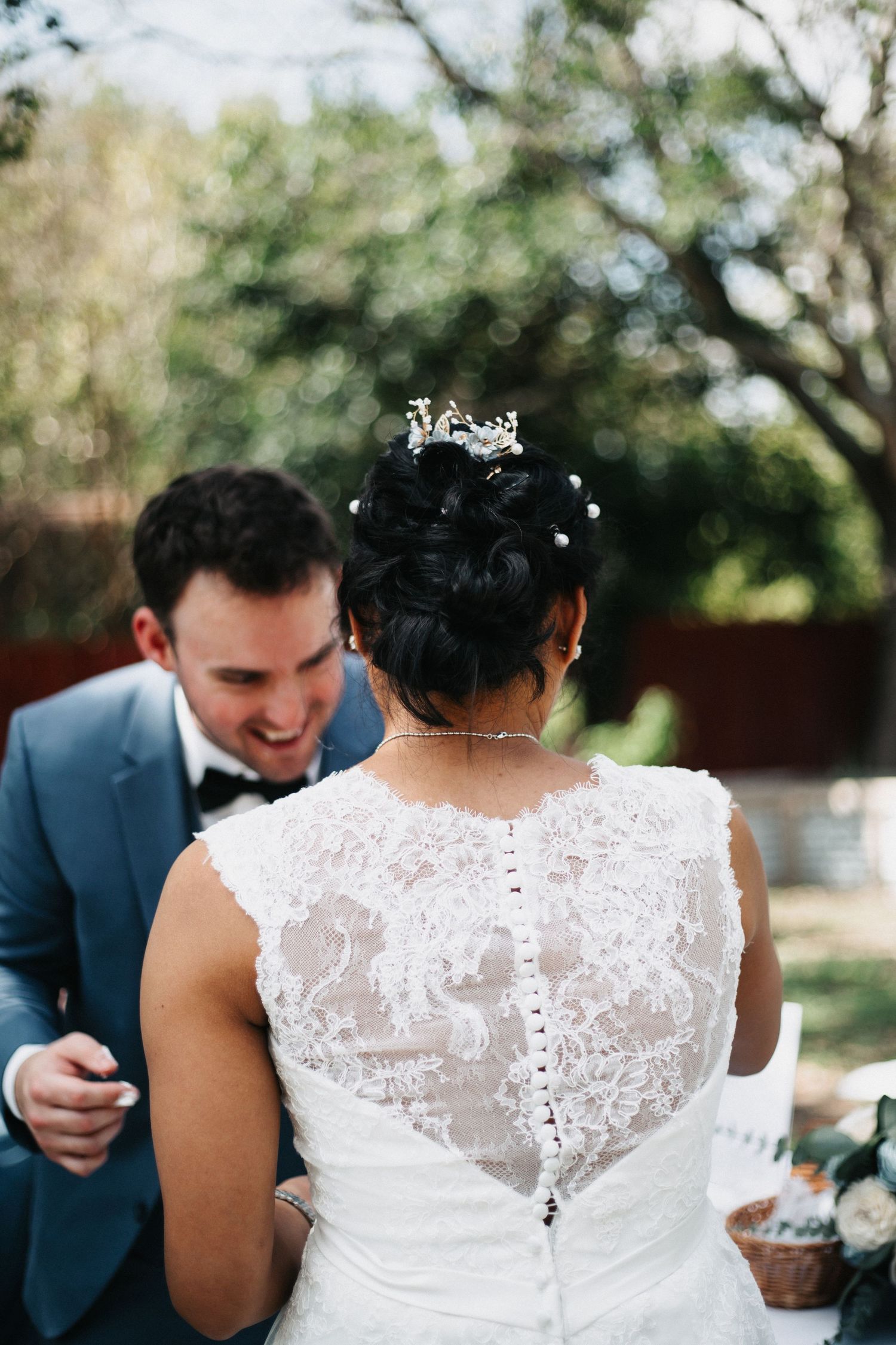 Intimate wedding moment captured from behind showing detailed lace back dress and blue suit.