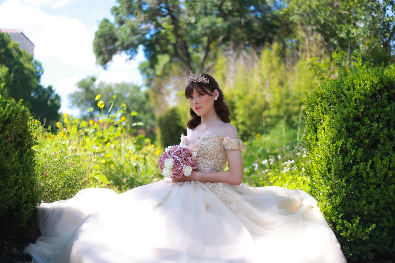 Dreamy garden portrait in a flowing white princess gown holding pink flowers.