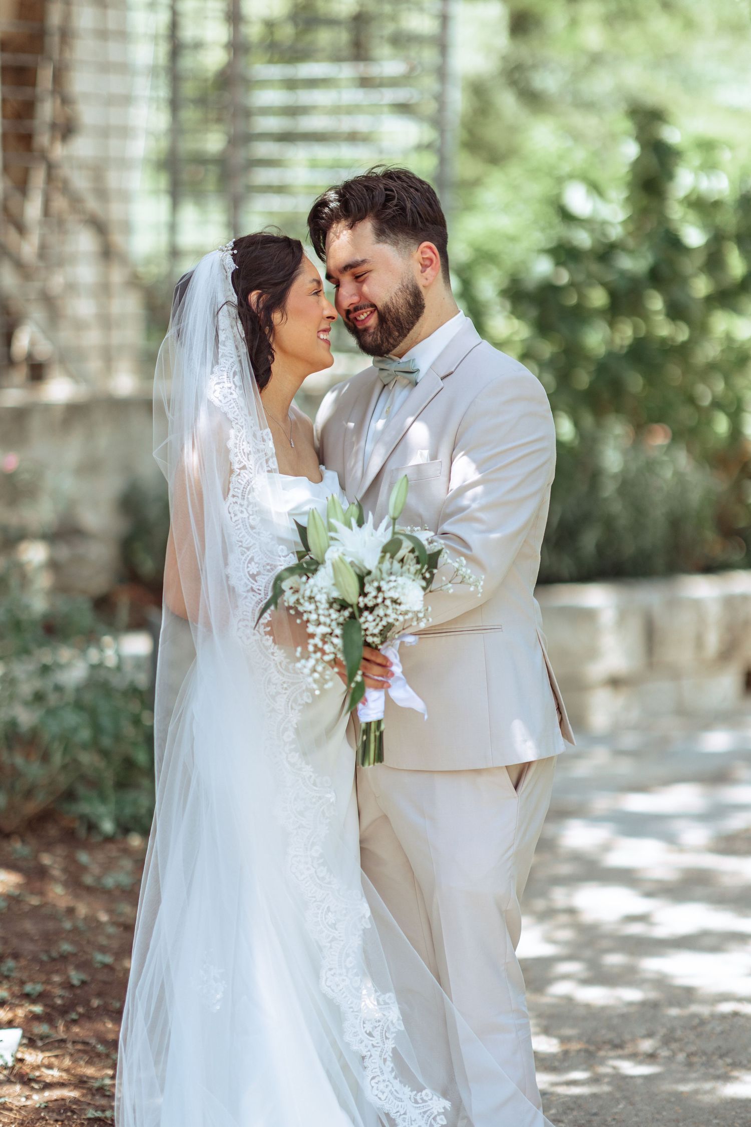 Romantic wedding portraits of couple embracing in dappled sunlight with white florals.