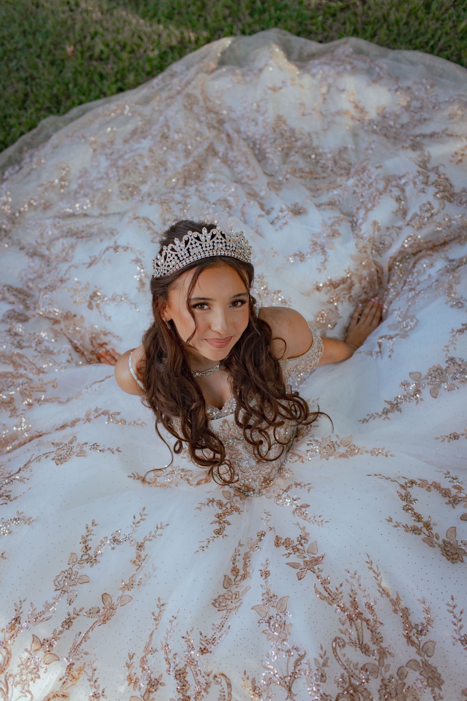 Luxurious white ball gown with rose gold embellishments displayed on green lawn with delicate details.
