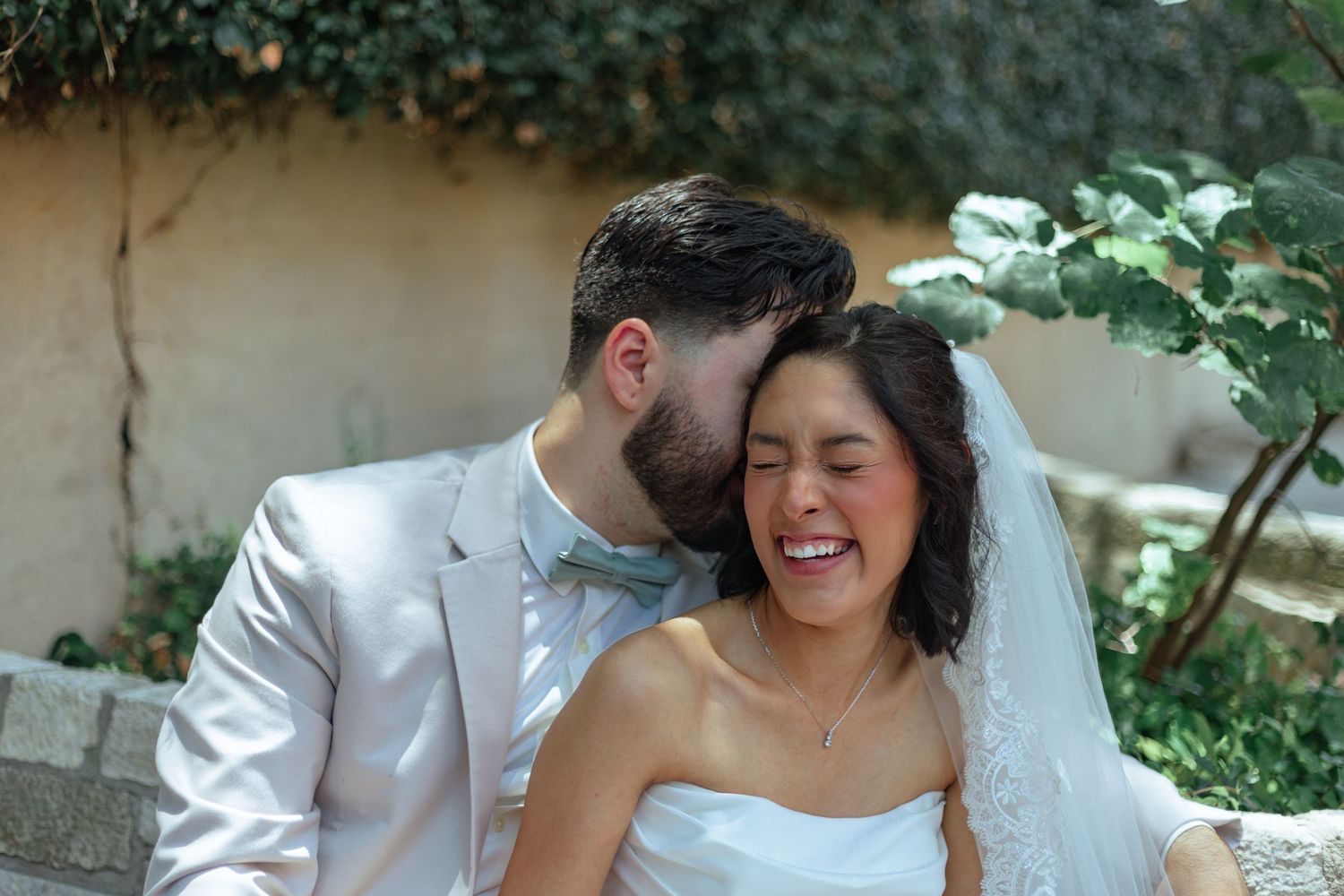 An intimate moment between newlyweds sharing laughter in a garden setting.