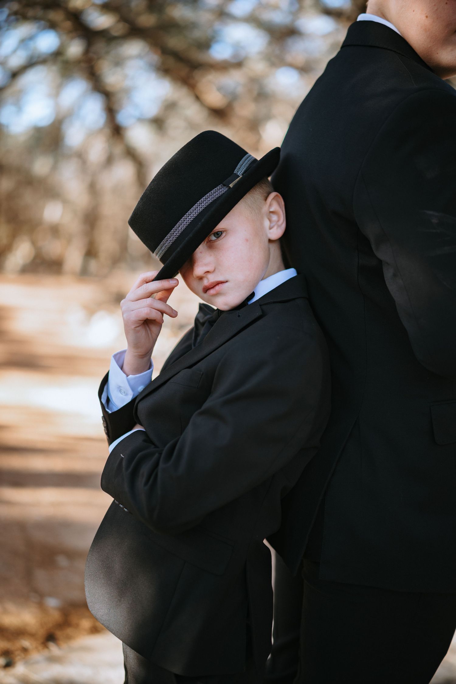 Young attendant in formal black suit and hat poses stylishly outdoors.