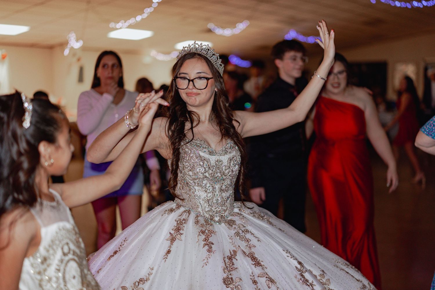 A celebration in a ballroom with people dancing, featuring someone in a glittering white quinceañera dress.