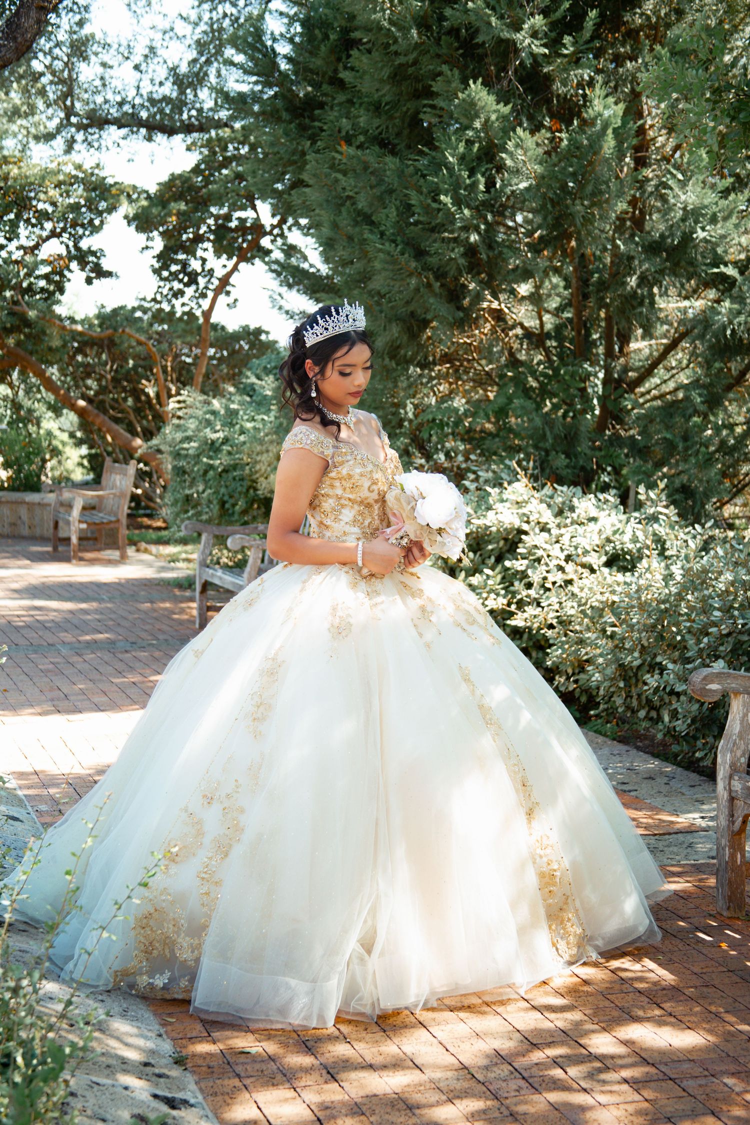 Ethereal outdoor photoshoot of cream and gold ballgown on brick pathway.