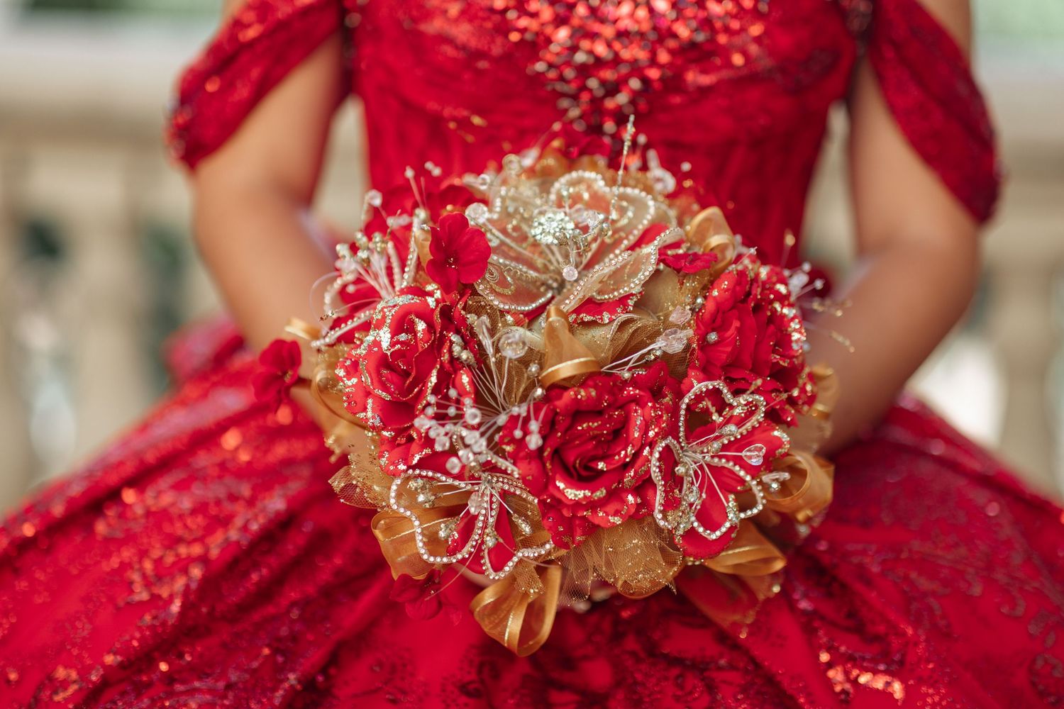 Close-up details of a sparkling red quinceañera dress with gold embellishments.