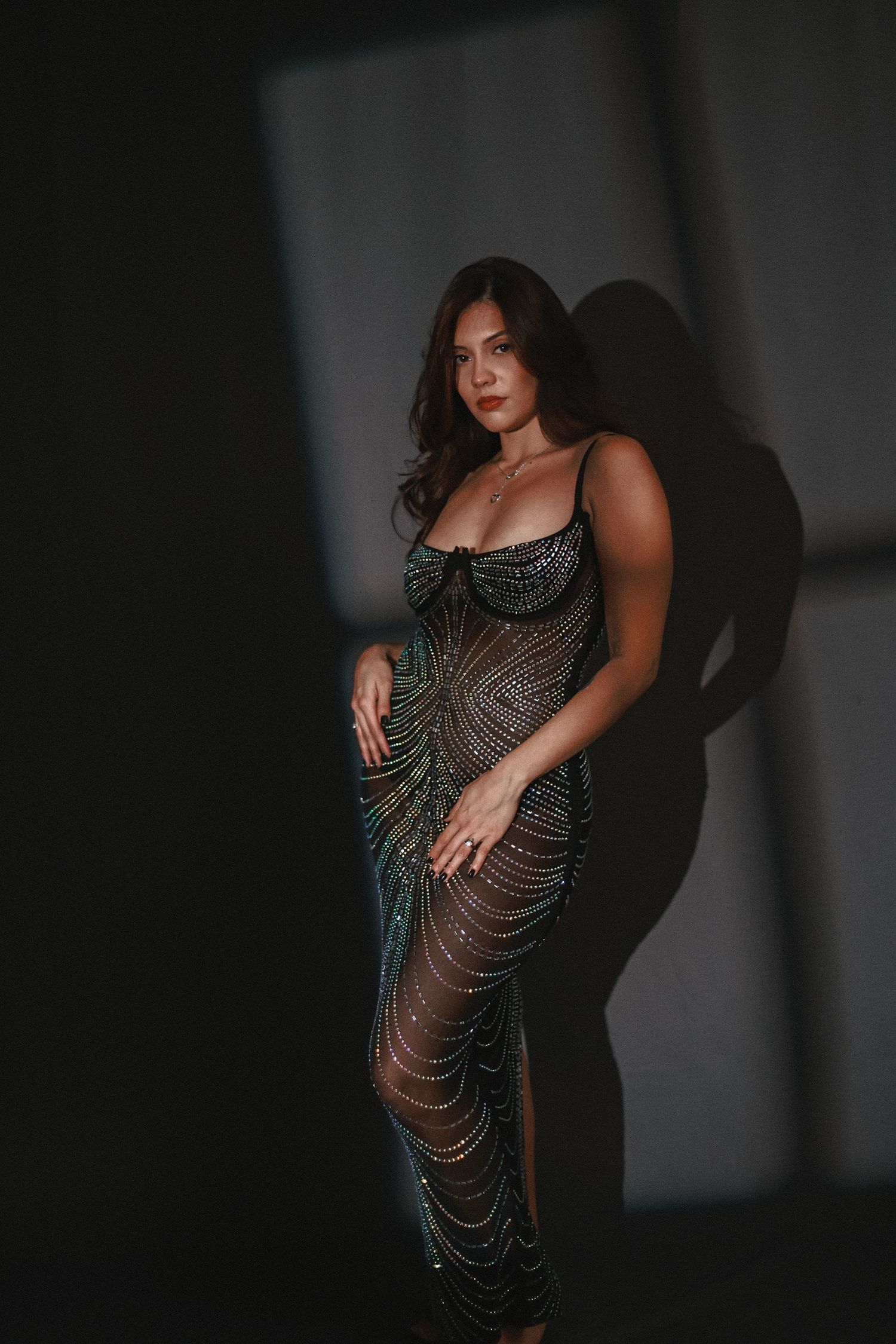 Model in shimmering beaded gown poses against dramatic dark background.
